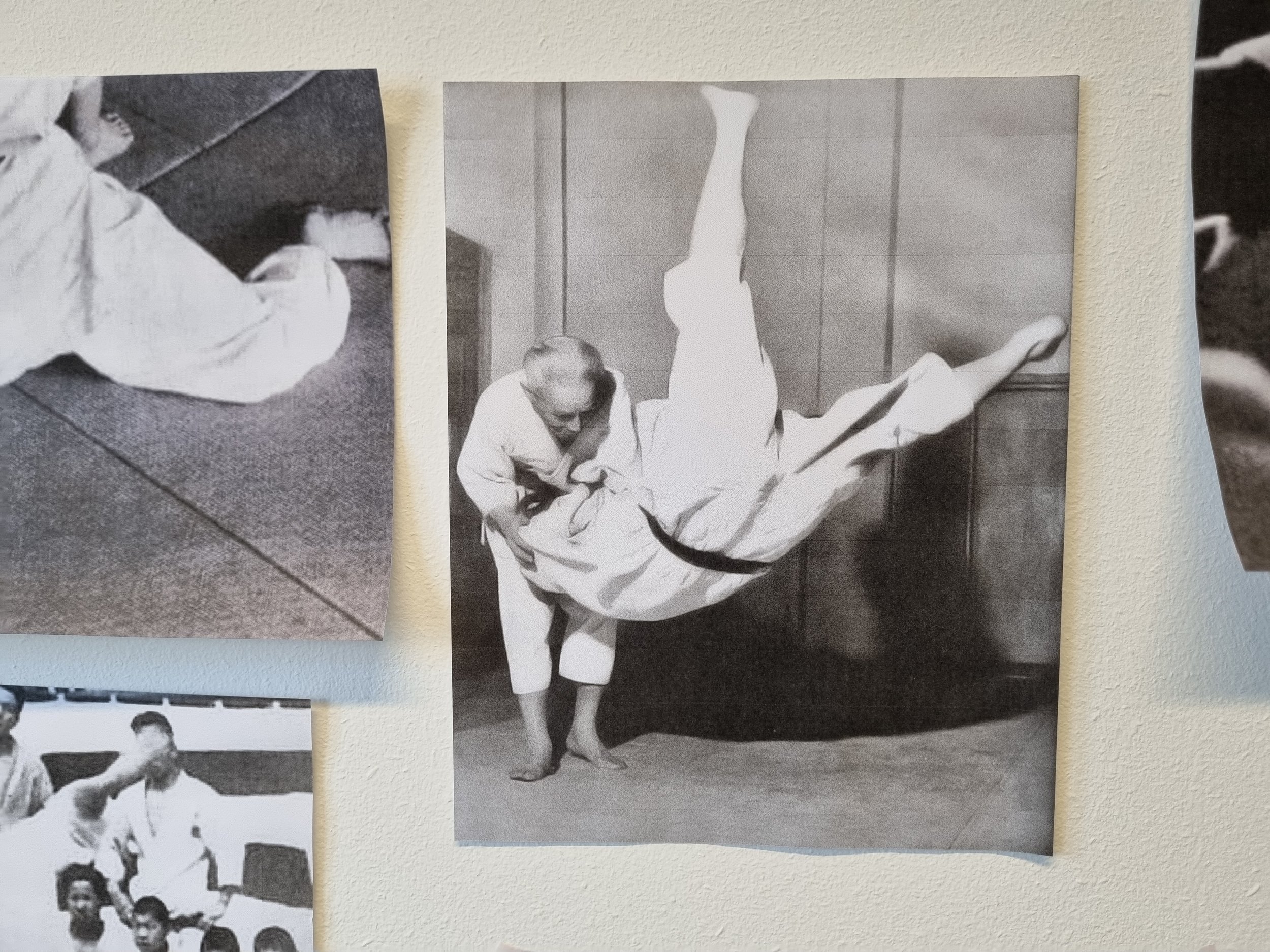 Black and white photocopy of an old judo master felling a young disciple in a spectacular yet controlled flip where the young man is suspended upside down in mid-air.