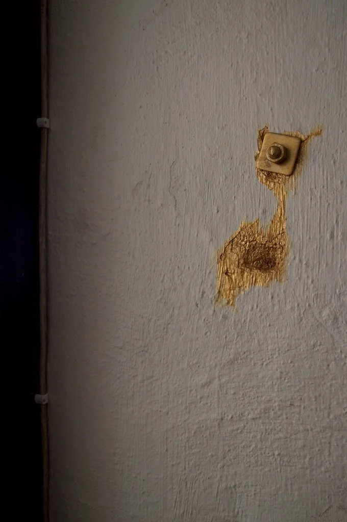 Two large screws on white plastered wall painted in gold enamel as part of site-specific art installation.