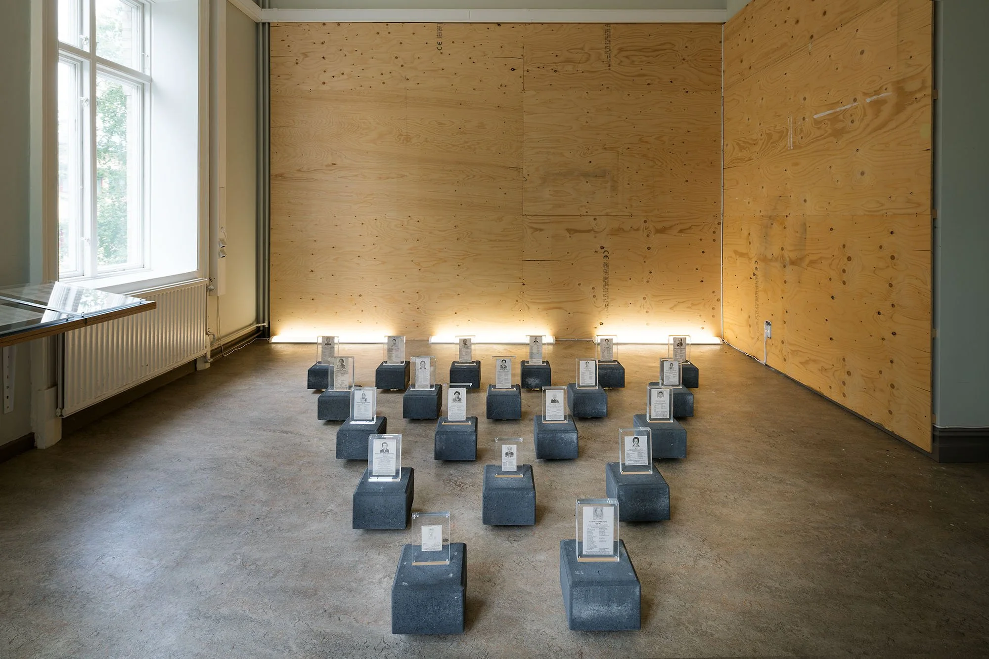 Full frontal image of a site-specific art installation with obituaries displayed on stone slabs on the floor in a tight formation.