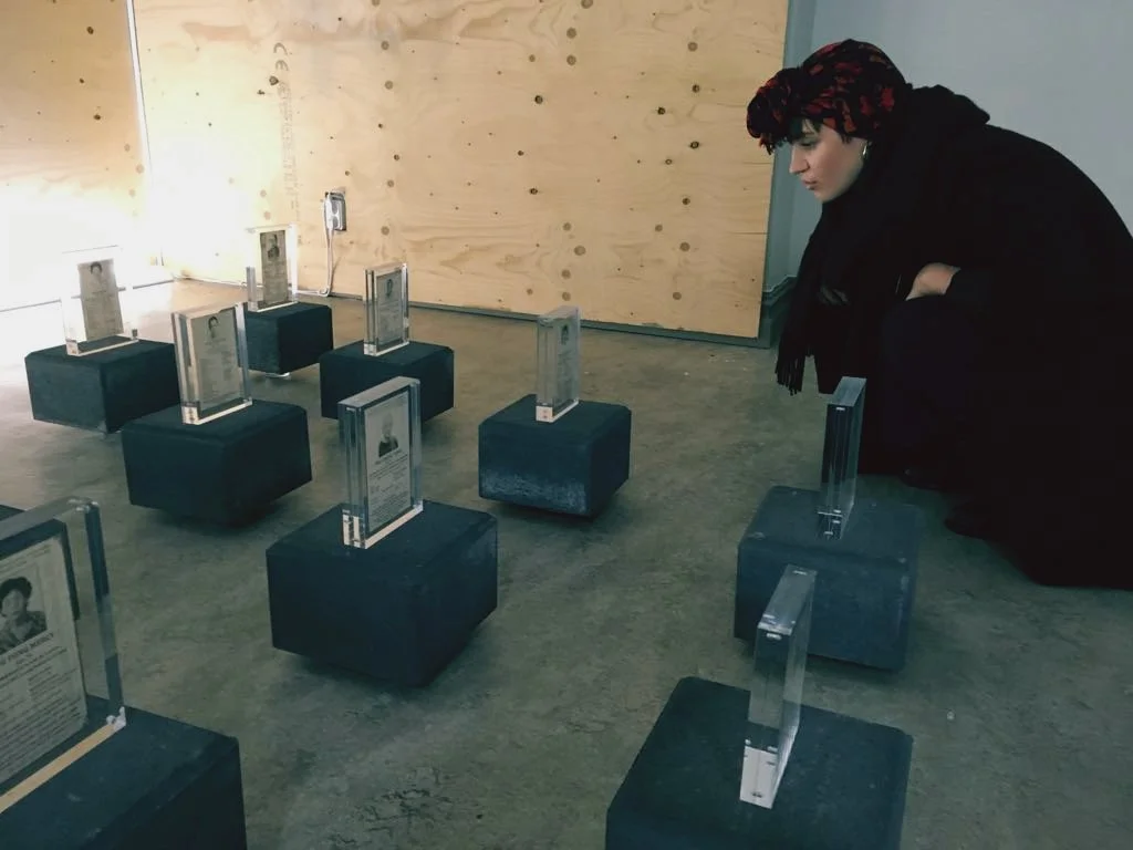 One female gallery visitor kneeling close to the installation on the floor to get a closer look at the images and texts on each of the displays.