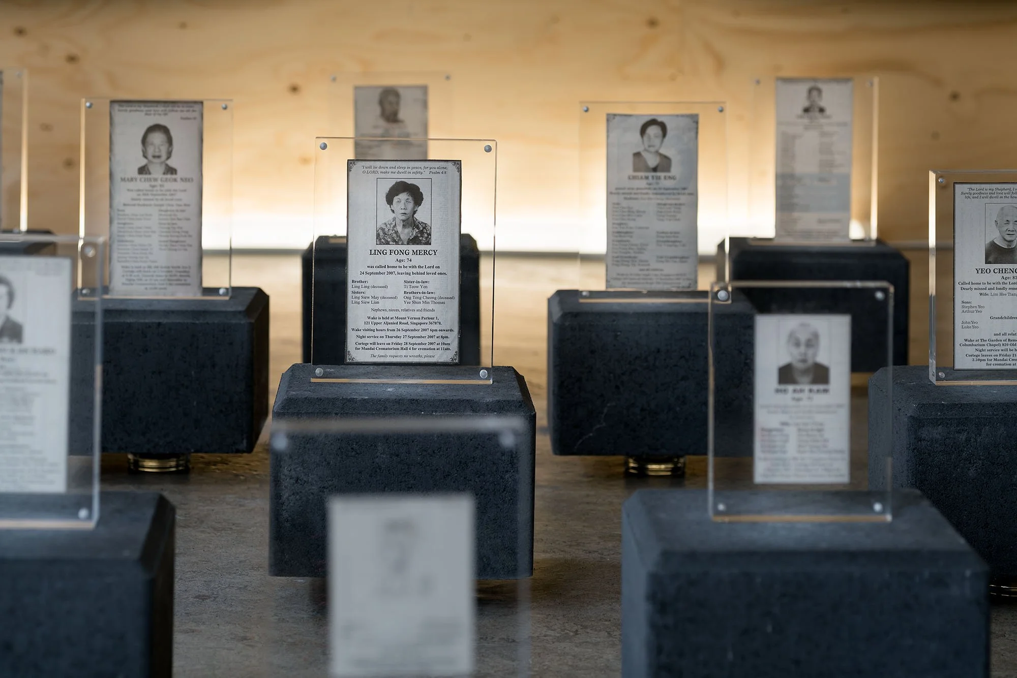 Close-up of the obituaries from the Straits Times displayed in individual plexi glass frames on a stone slab.