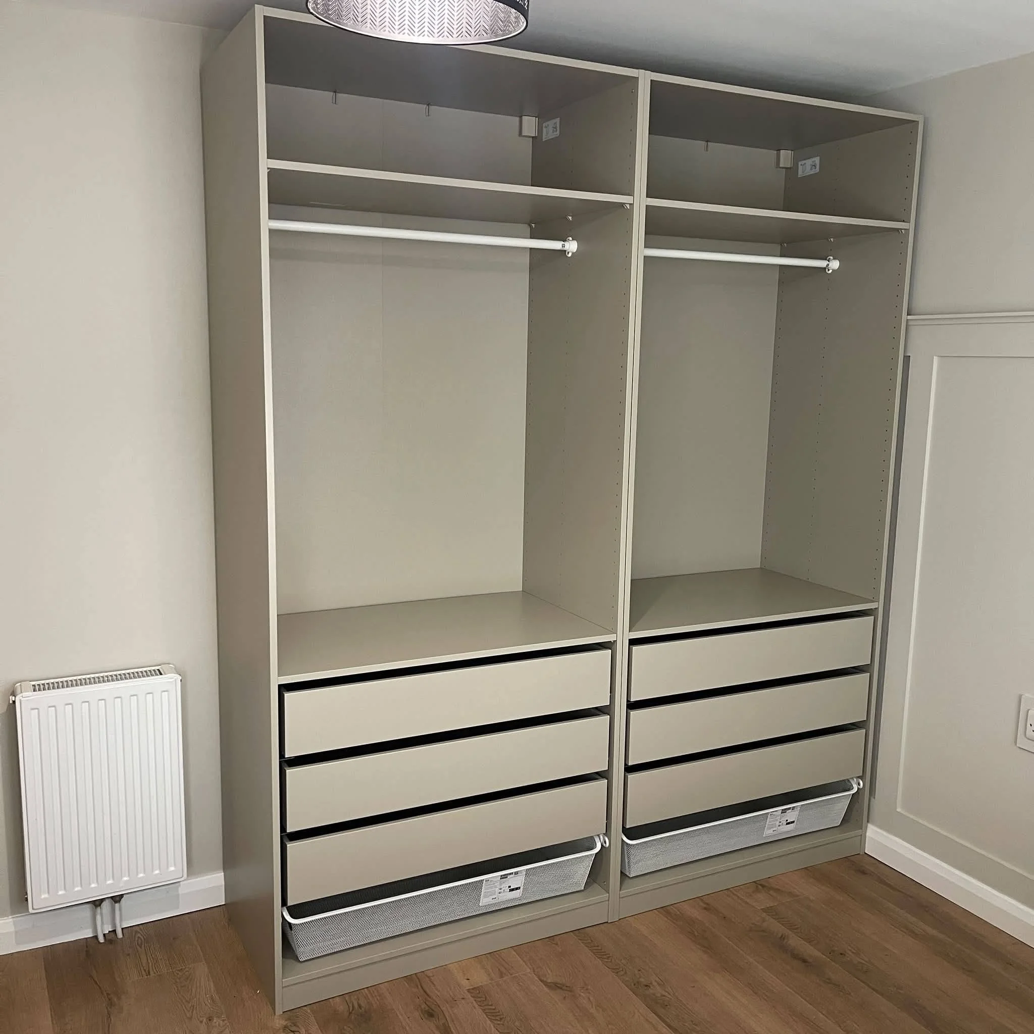 Empty white and gray shelving unit with multiple compartments, located in a room with wooden flooring and plain white walls.