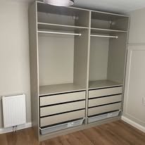 Empty wardrobe with two sliding doors, shelves, and drawers inside, located in a room with hardwood floor.