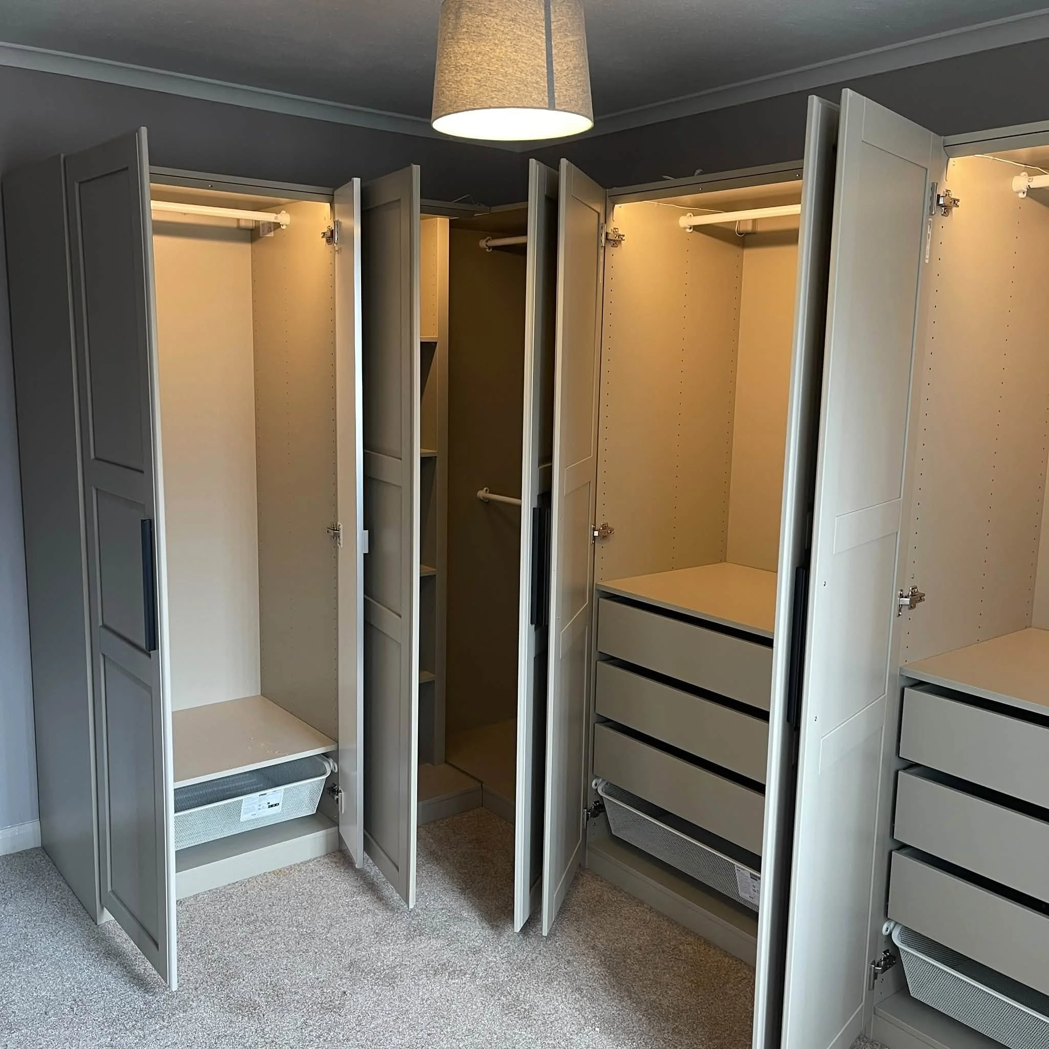 Empty built-in white closet with open doors, shelving, and hanging rods in a room with beige carpet and a ceiling light fixture.
