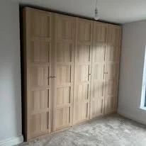 Wooden closet with multiple doors in a room with a window.