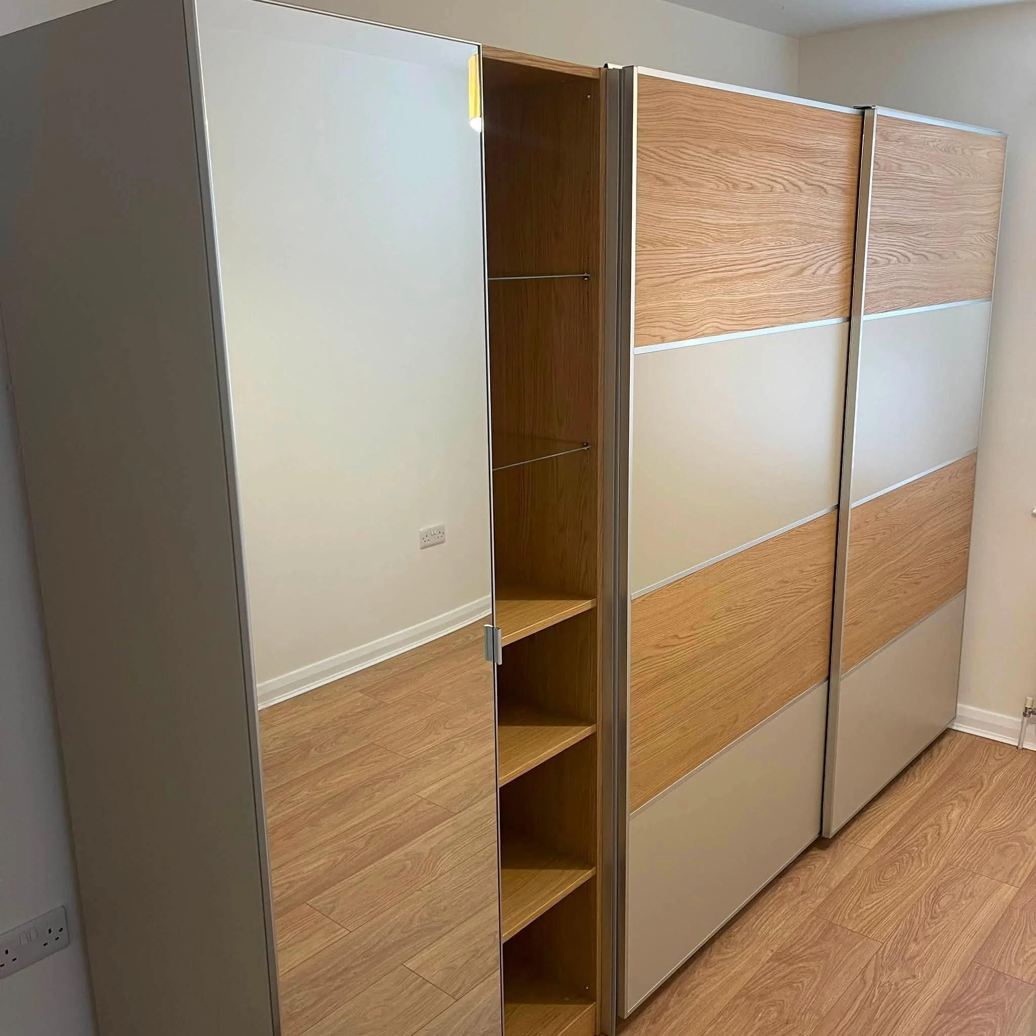 Empty wooden and gray metal closet with sliding doors in a room with wooden floor.