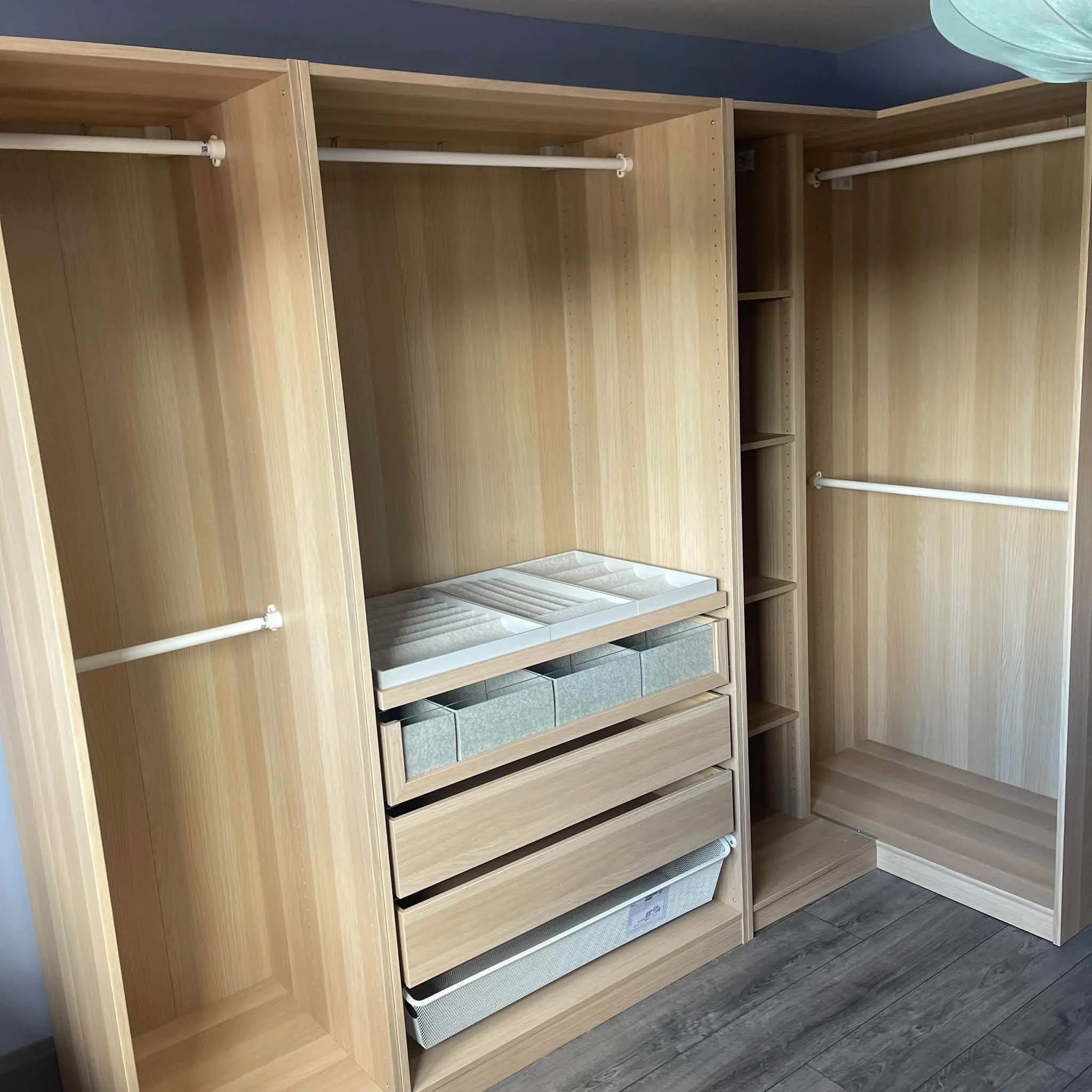 Wooden closet with open shelves, hanging rods, and a lower shelving area, situated in a room with gray flooring and painted walls.