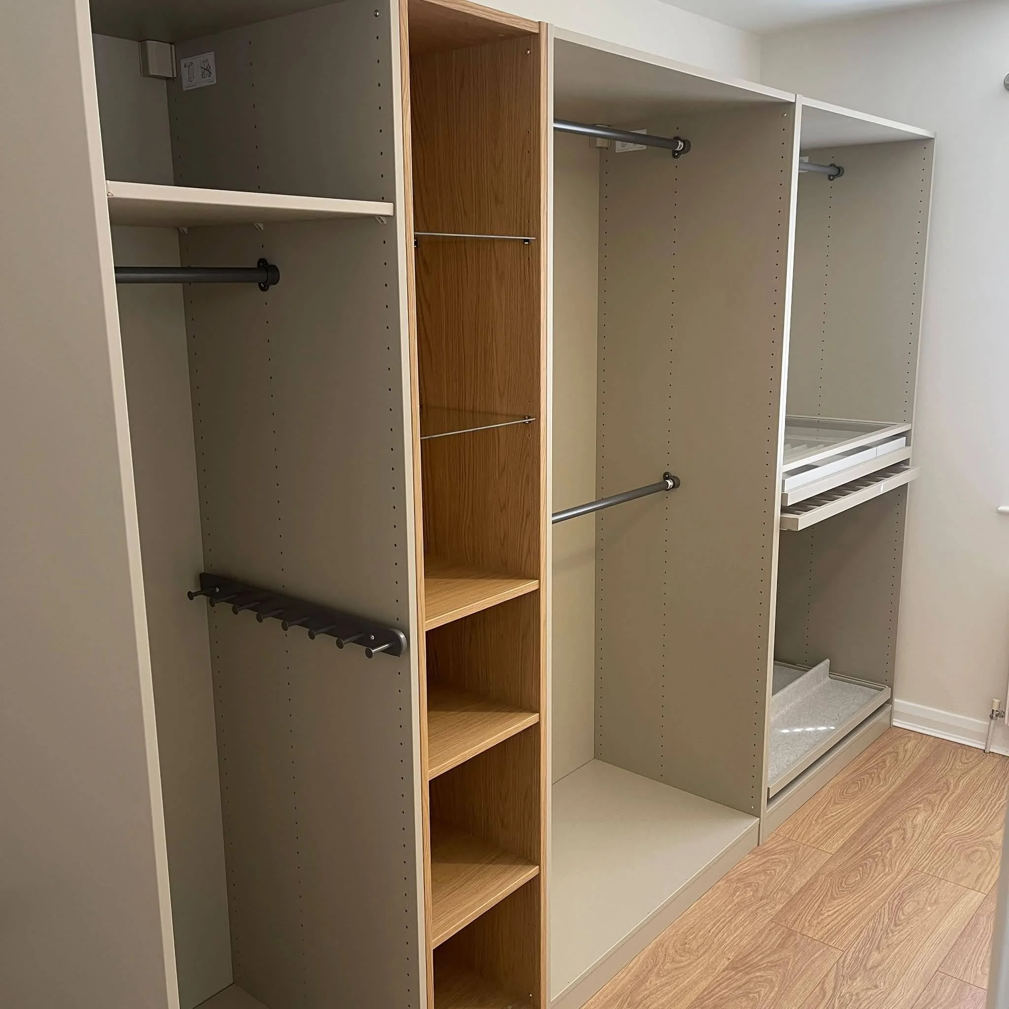 Empty built-in closet with white and wood finish, multiple shelves and hanging rods, installed along a wall with hardwood flooring.