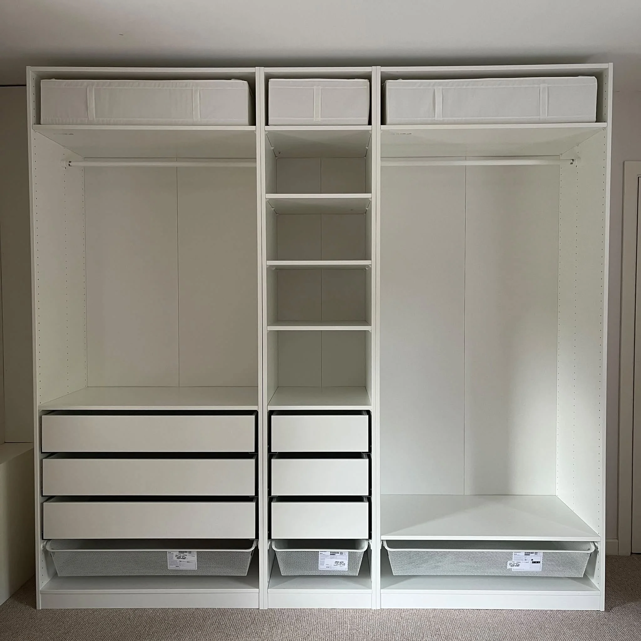 Empty white shelving unit with baskets on top and bottom, located indoors on a beige carpet.