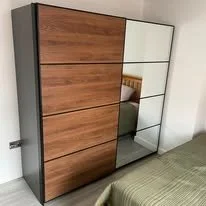 A modern wardrobe with a sliding door, partially mirrored, next to a bed with a bedpost visible.