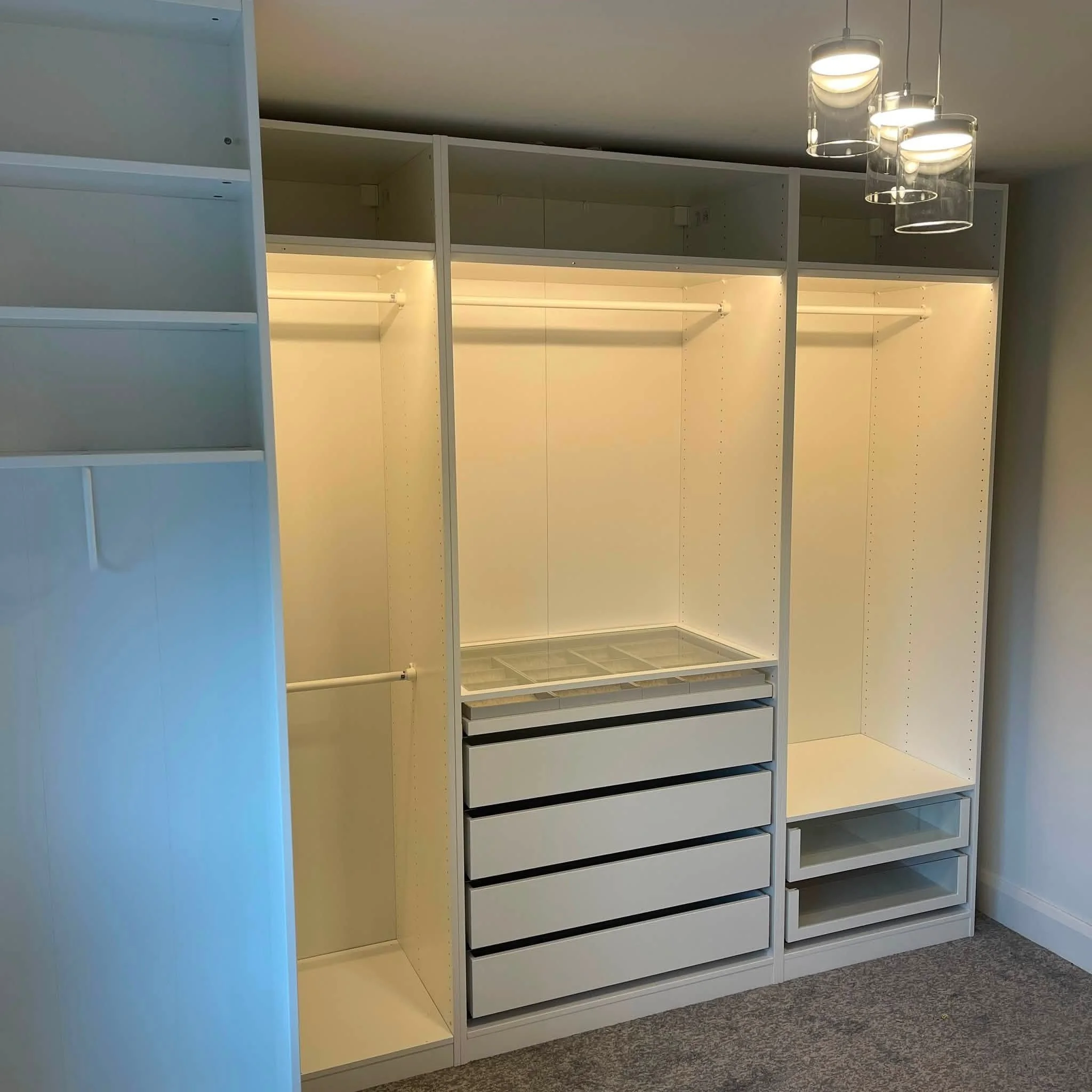 Empty white shelving unit with lights inside, set up for office or wardrobe storage, located on a carpeted floor with a ceiling light fixture overhead.