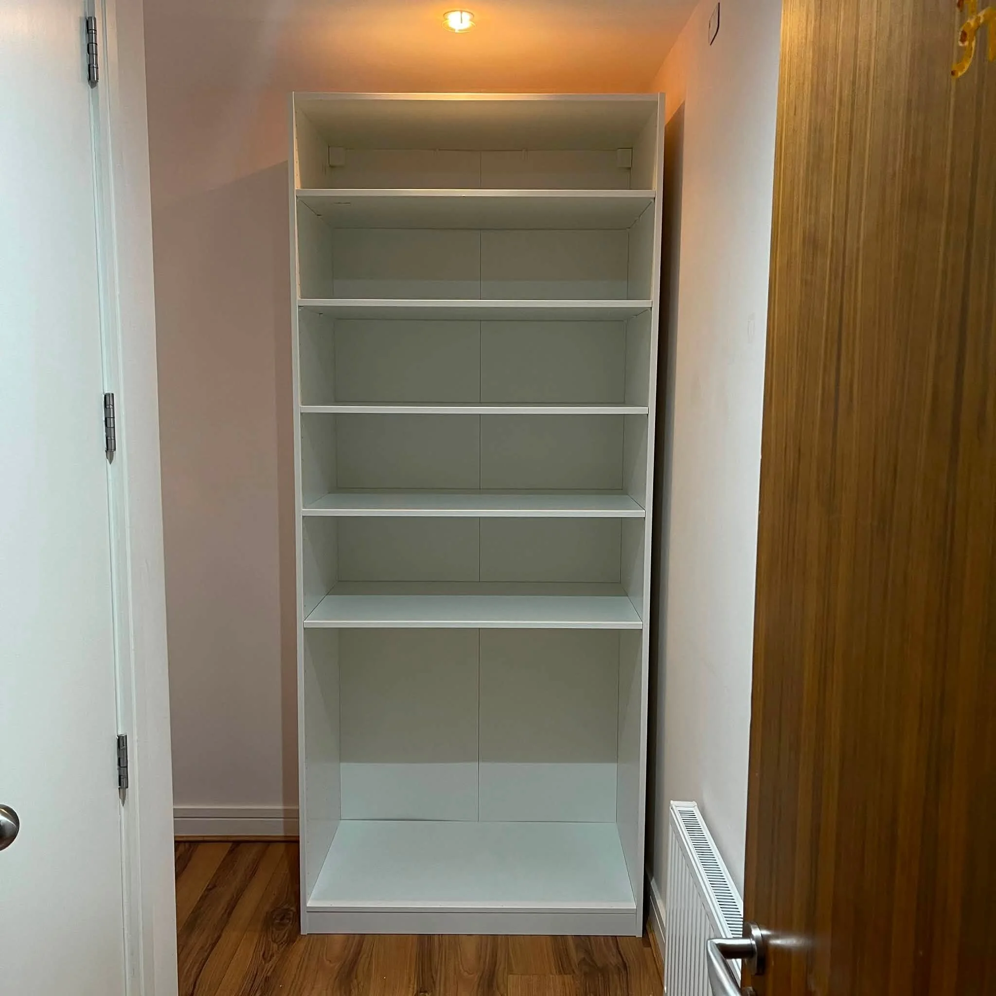 Empty white bookshelf with four compartments, situated on a hardwood floor against a beige wall.