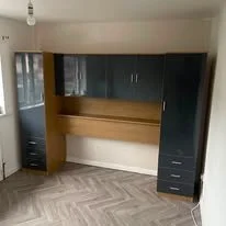 A built-in desk unit with cabinets and drawers, situated in a room with wood-patterned flooring and a window.