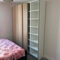 Empty white bookshelf with multiple shelves next to a bedroom with a bed and floral bedspread.