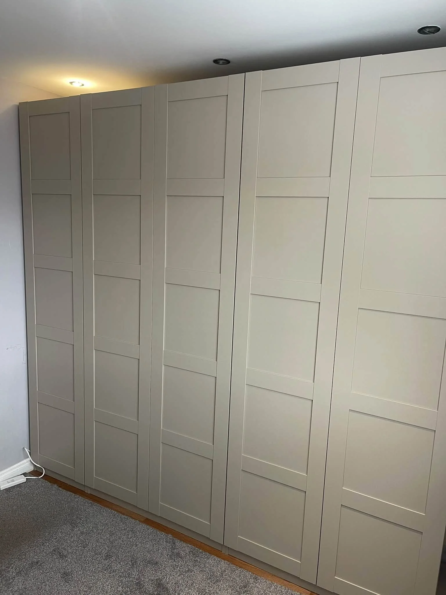 A large beige wardrobe with multiple panels in a room with gray carpet and a white wall.