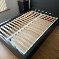 Empty black bed frame with wooden slats and metal support bar in a bedroom