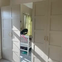 Bright bedroom with a crib and a window with curtains, partially obscured by a closet door.