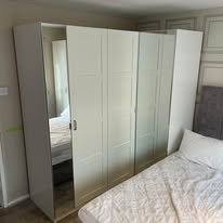 A white four-door wardrobe next to a bed in a bedroom.