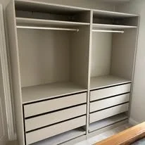 Empty white closet with shelves, drawers, and hanging rods.