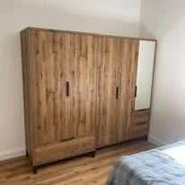 A wooden wardrobe with sliding doors, one of which has a mirror, positioned against a white wall in a bedroom.