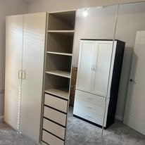 A set of white storage cabinets and shelves in a room, with some open shelves and drawers, and a small refrigerator or cabinet unit.