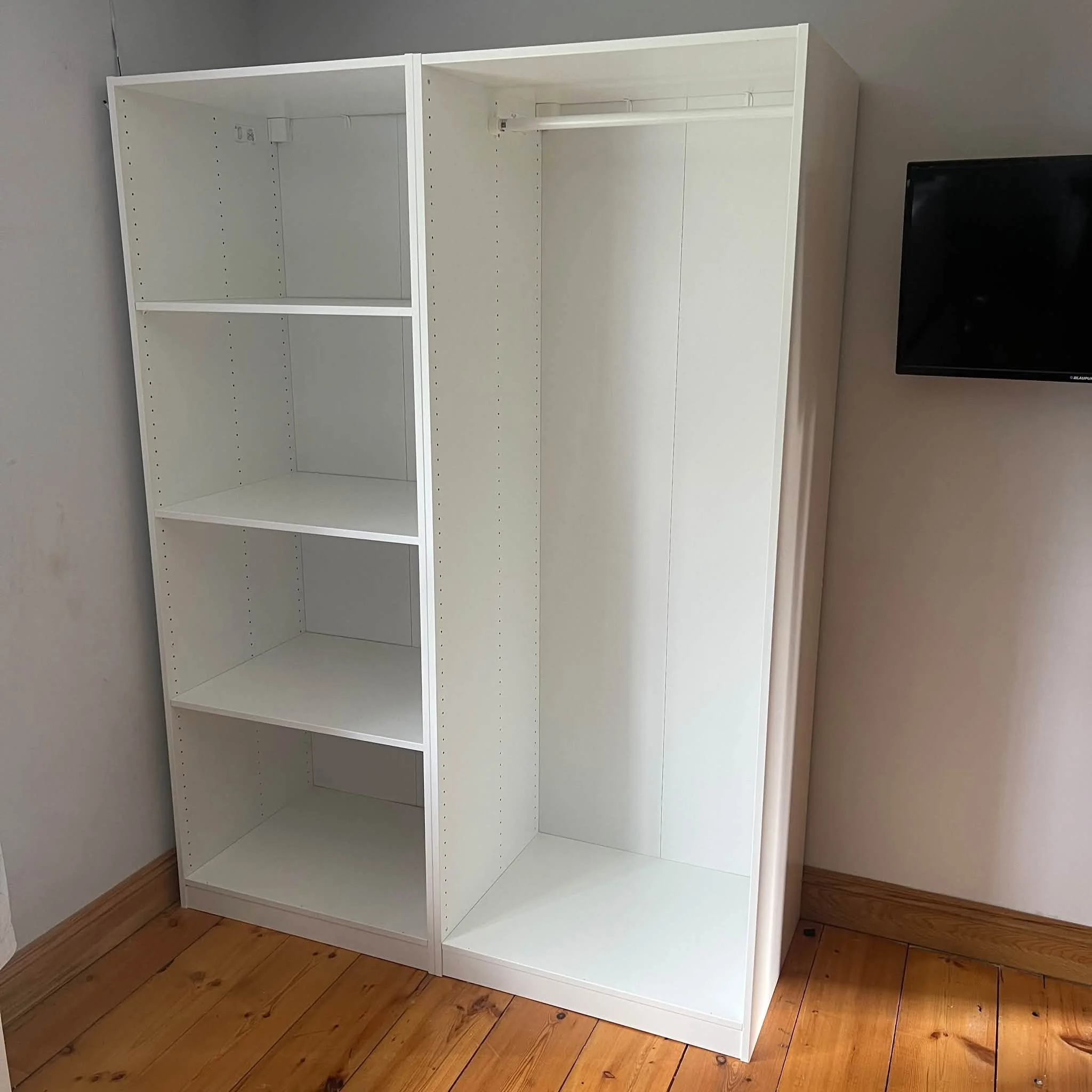 Empty white bookshelf with three shelves against a gray wall on a wooden floor.