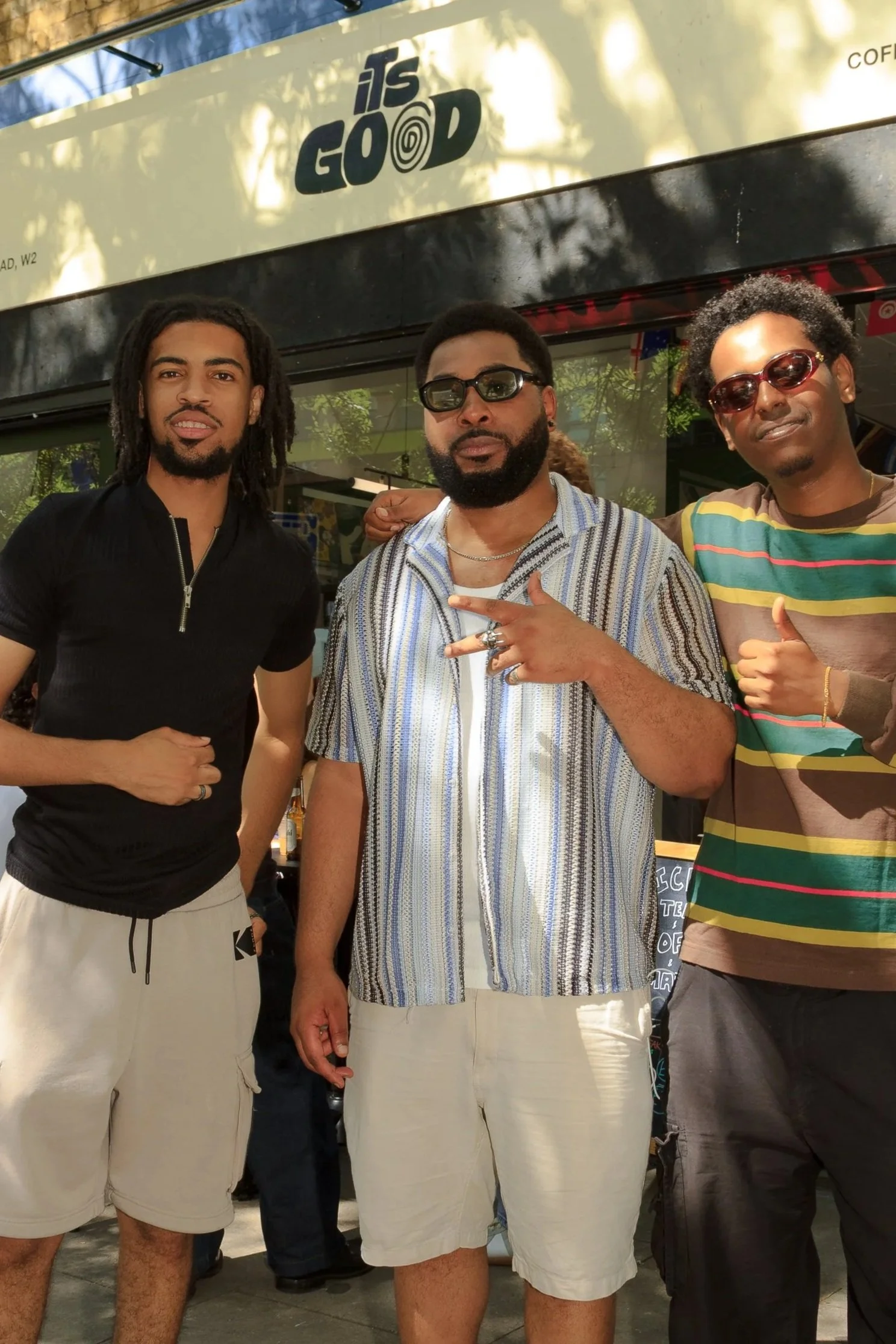 Three men standing outside in front of a cafe with the sign reading ‘It’sGood.’ They are posing for the photo.