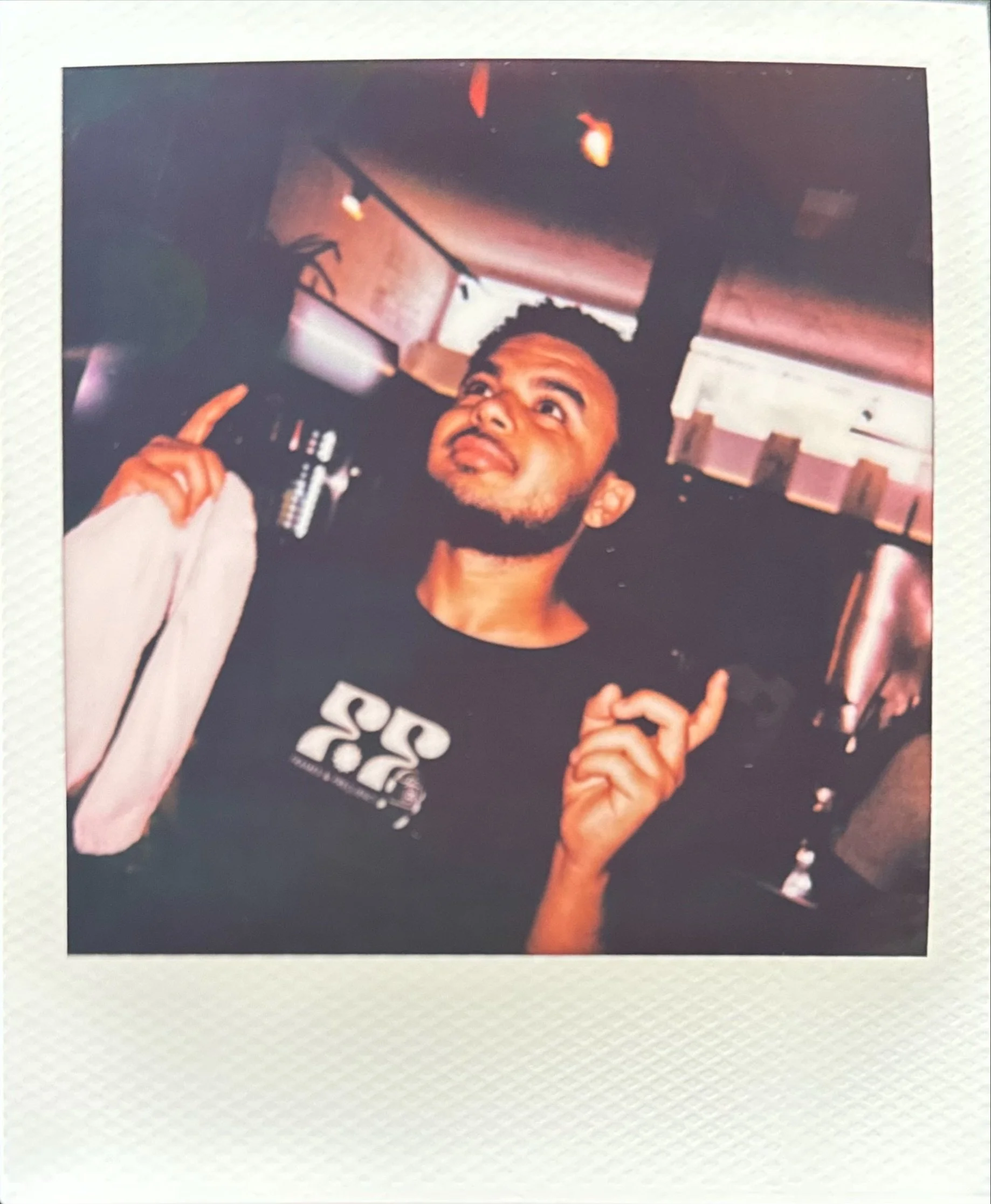Bearded man in a black graphic T-shirt making a hand gesture inside a dimly lit car