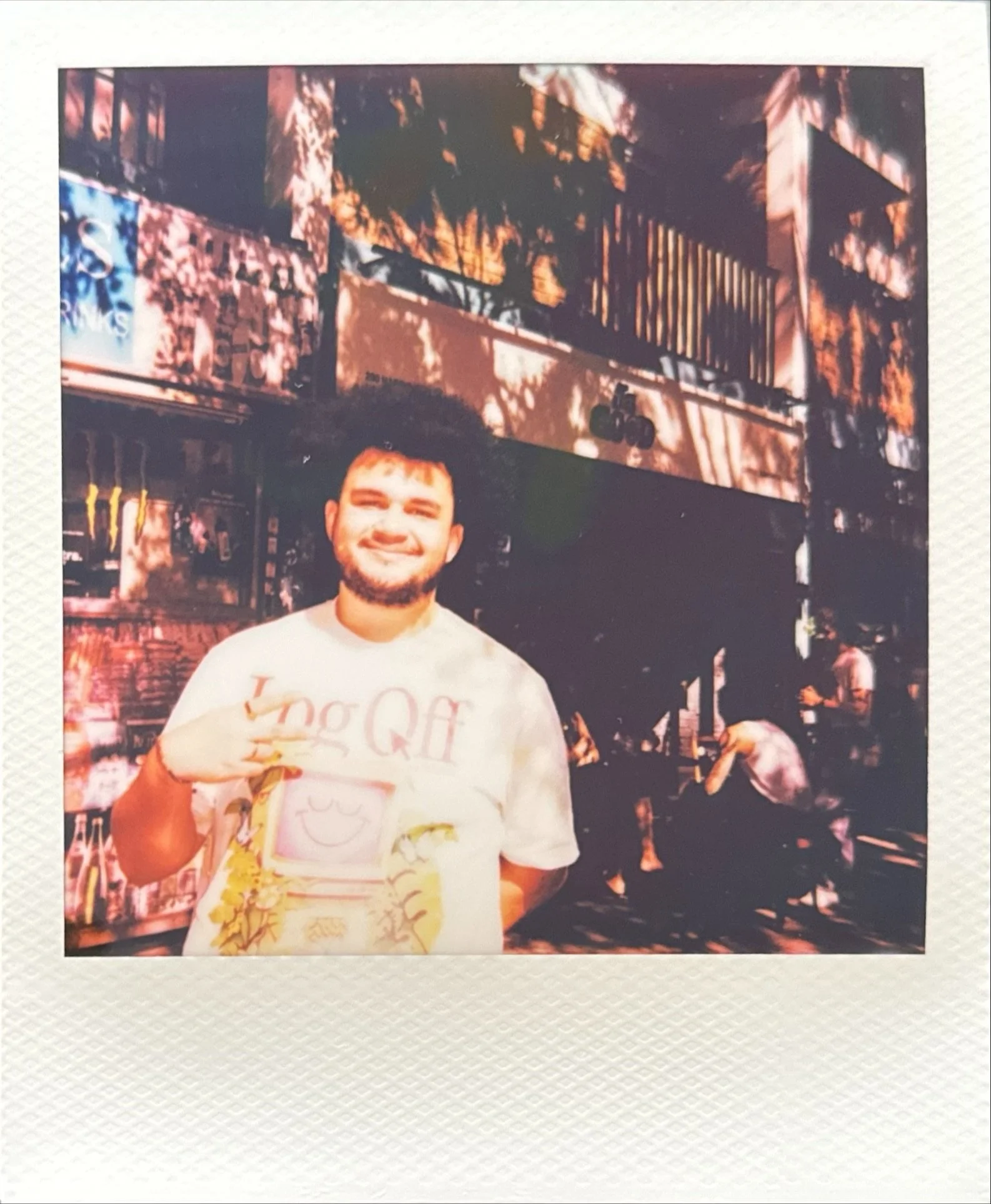 Smiling man in a graphic T-shirt posing outside a restaurant or bar at night.
