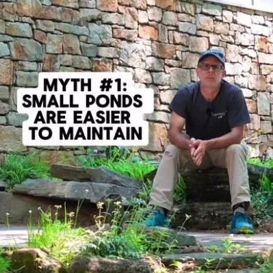 A person sitting outdoors in front of a stone wall, wearing a dark t-shirt, khaki pants, and a cap, next to a sign that reads 'Myth #1: Small ponds are easier to maintain' with greenery around them.