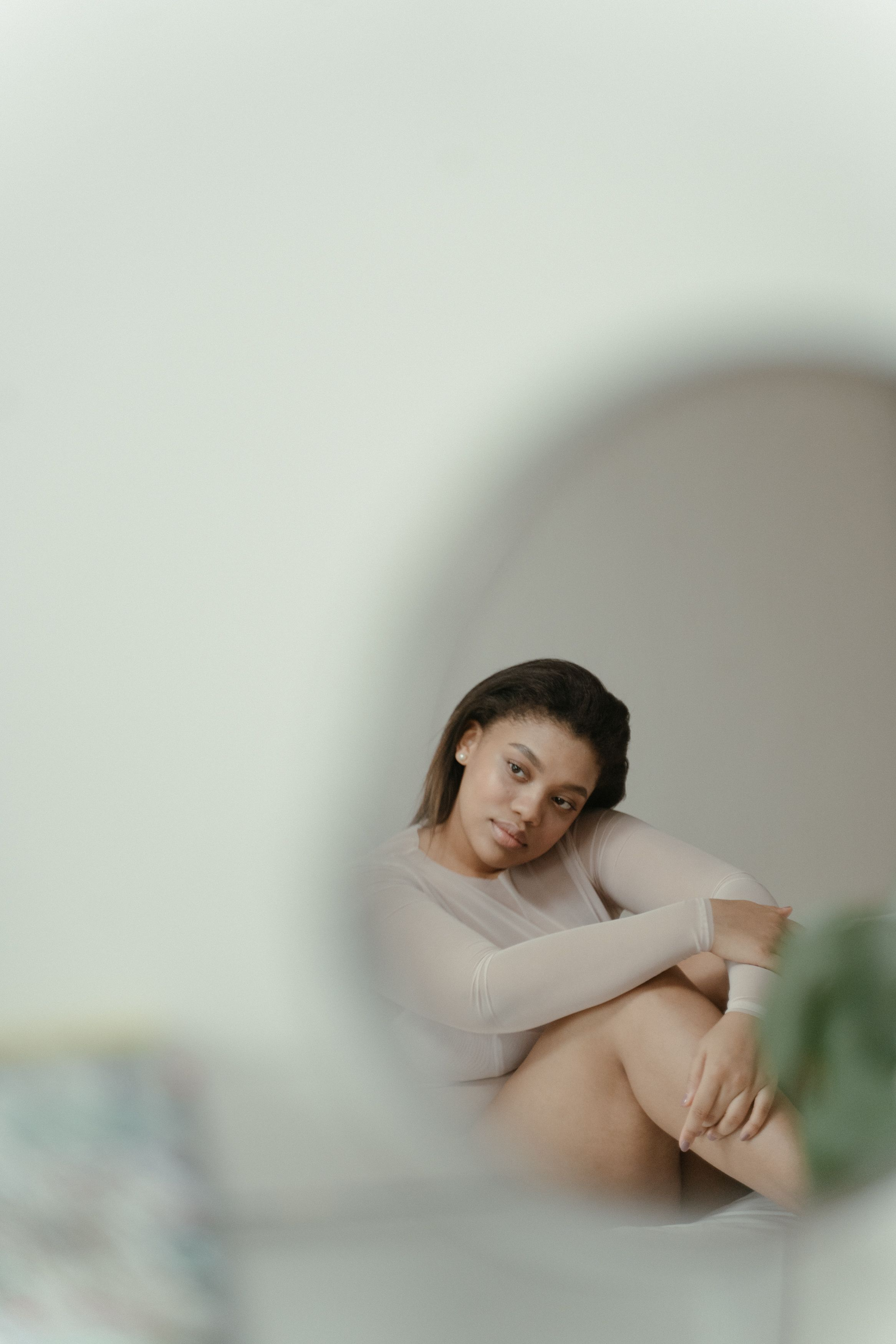A woman with dark hair and light brown skin, sitting with her arms crossed over her knees, in a neutral room with minimalist decor.