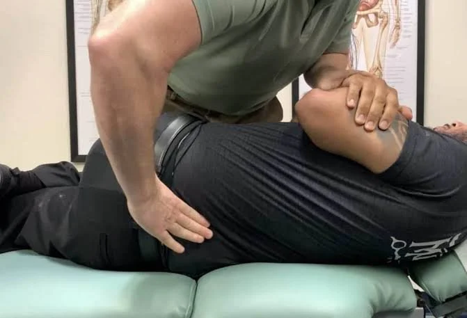 A healthcare professional performing a chiropractic adjustment on a patient lying face down on a medical table.