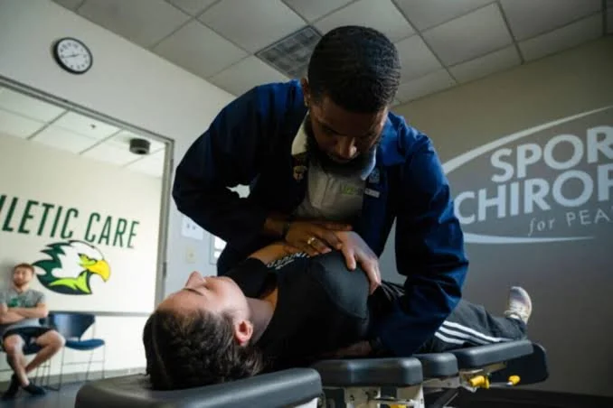 Chiropractor adjusting a patient's shoulder in an athletic care clinic with a logo for Sports Chiropractic.