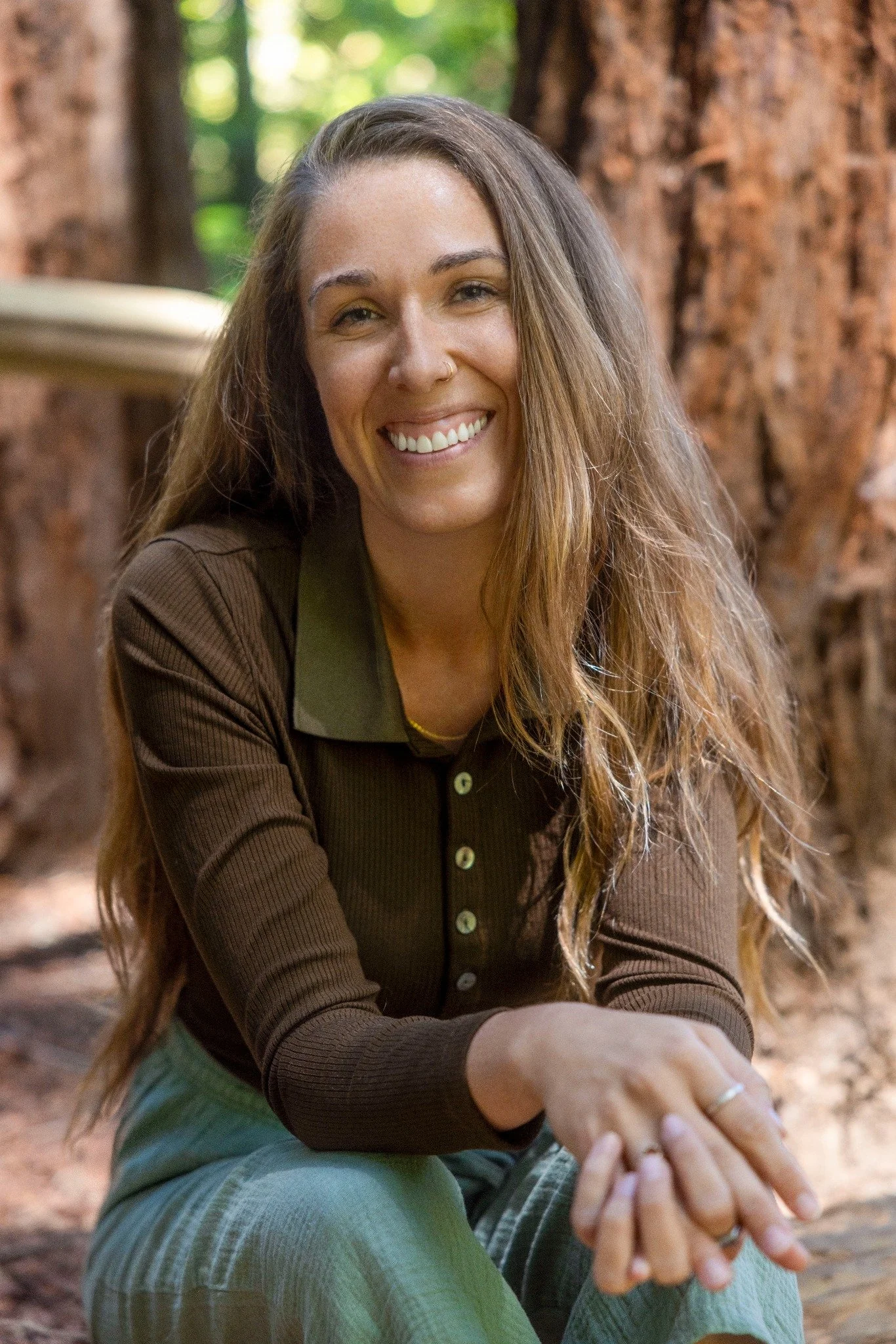 Angela Soley, LMFT, smiling and seated outdoors among redwood trees