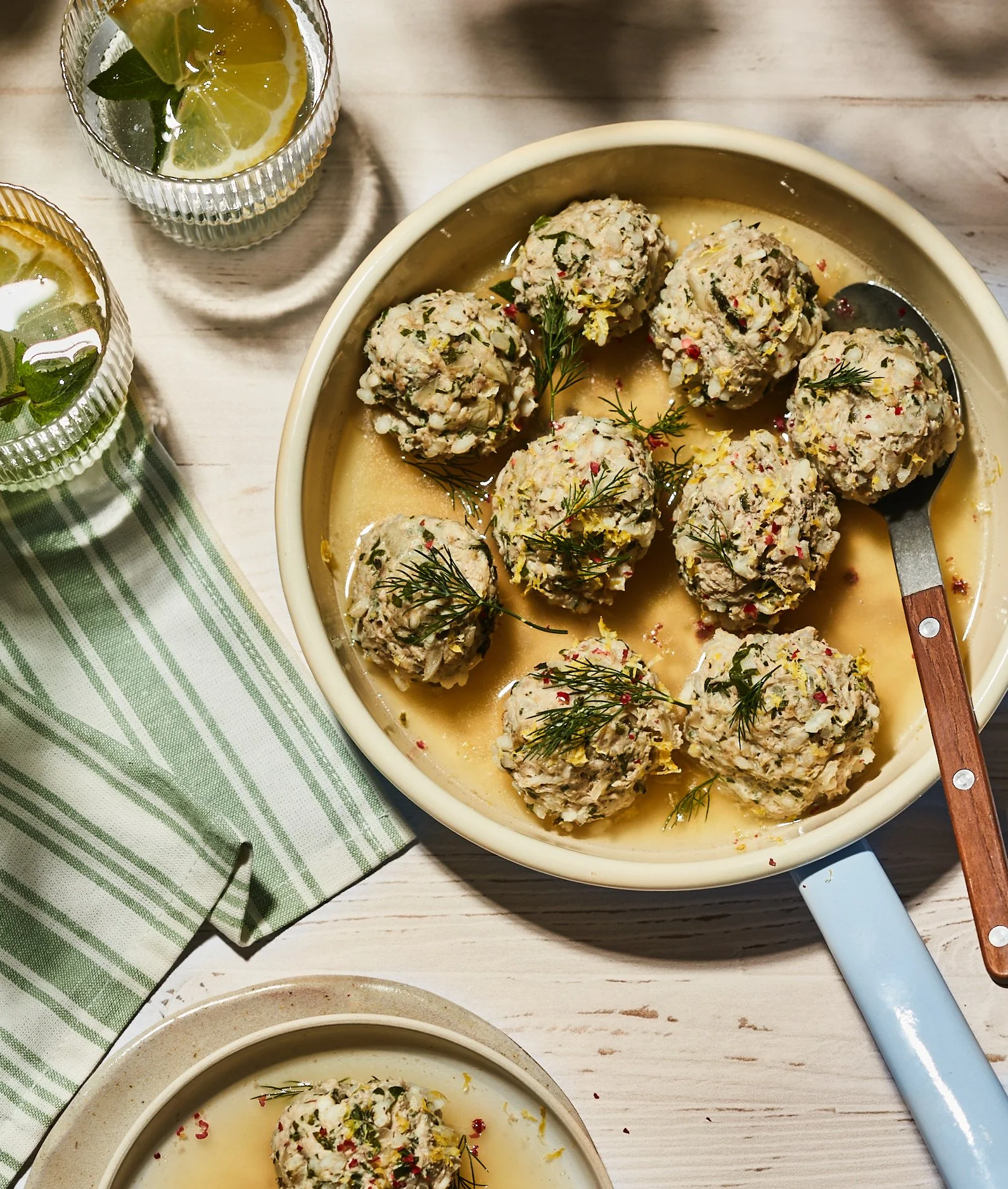 Boules de fromage frais assaisonnées, garnies d'herbes et d'épices, dans une casserole avec une sauce, accompagnées de verres de boissons citronnées à la menthe, sur une table en bois