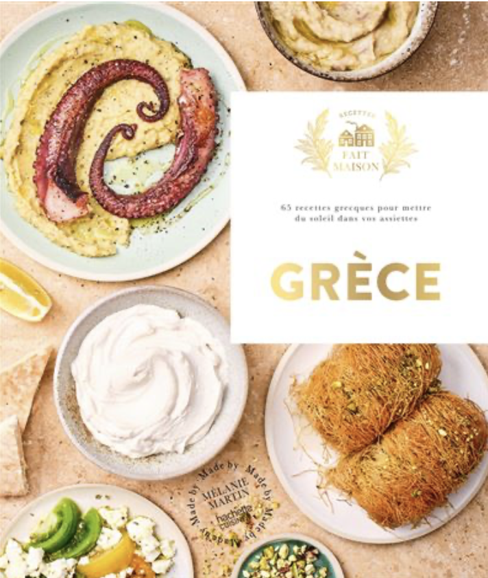 Livre de recettes grecques avec plats traditionnels comme calamars, tzatziki, et dolmas, sur une table en marbre