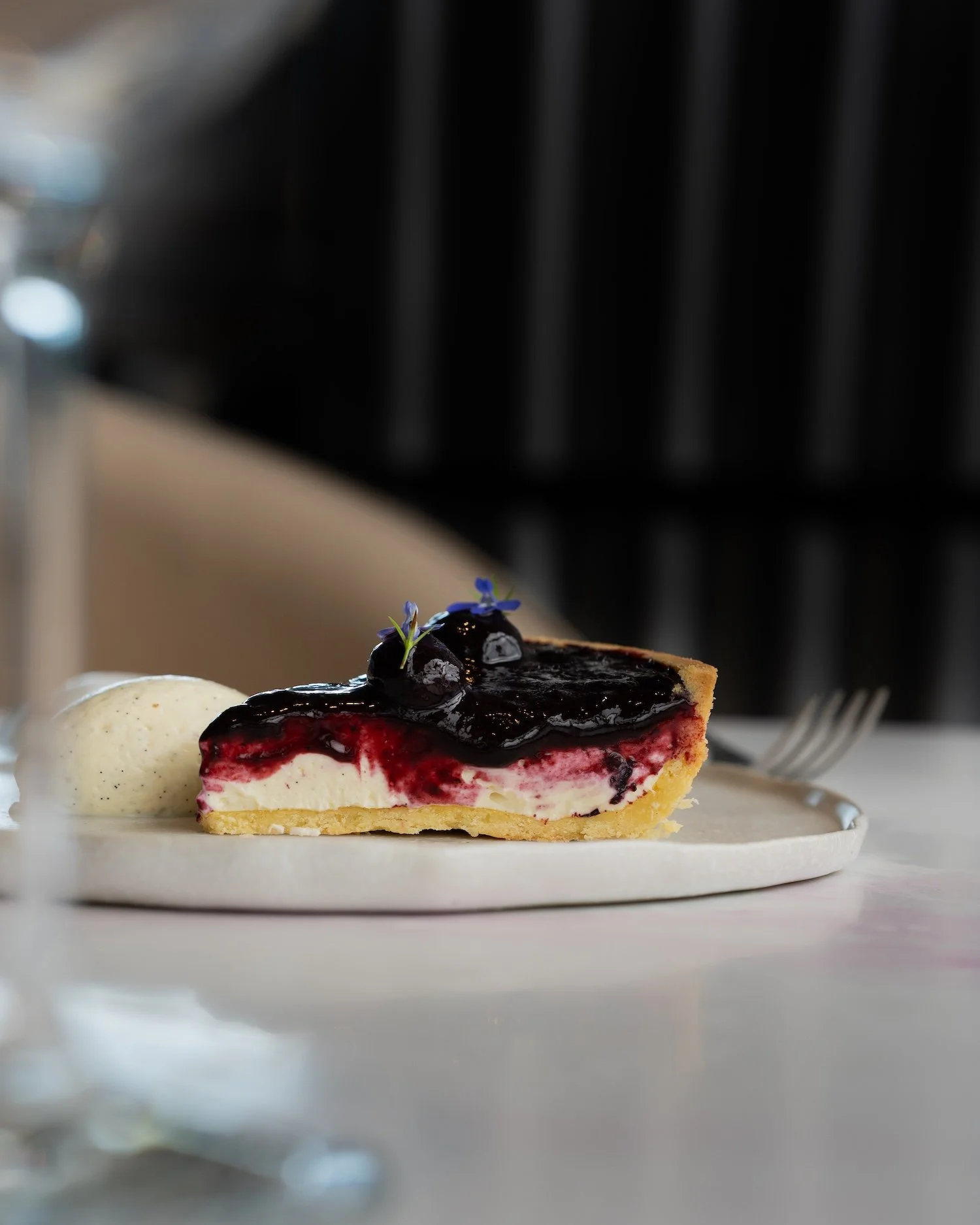 Une part de tarte aux fruits rouges avec une sauce brillante sur le dessus, accompagnée d'une boule de glace à la vanille au côté, servie sur une assiette blanche.
