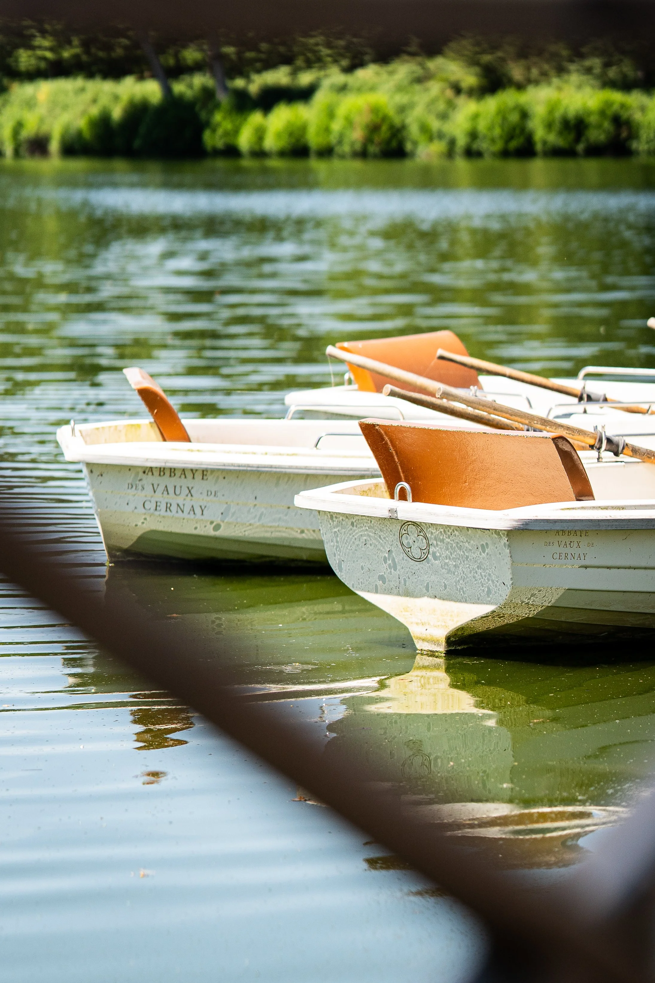 Bateaux en bois orange et blanc flottant sur un lac avec des arbres verts en arrière-plan.