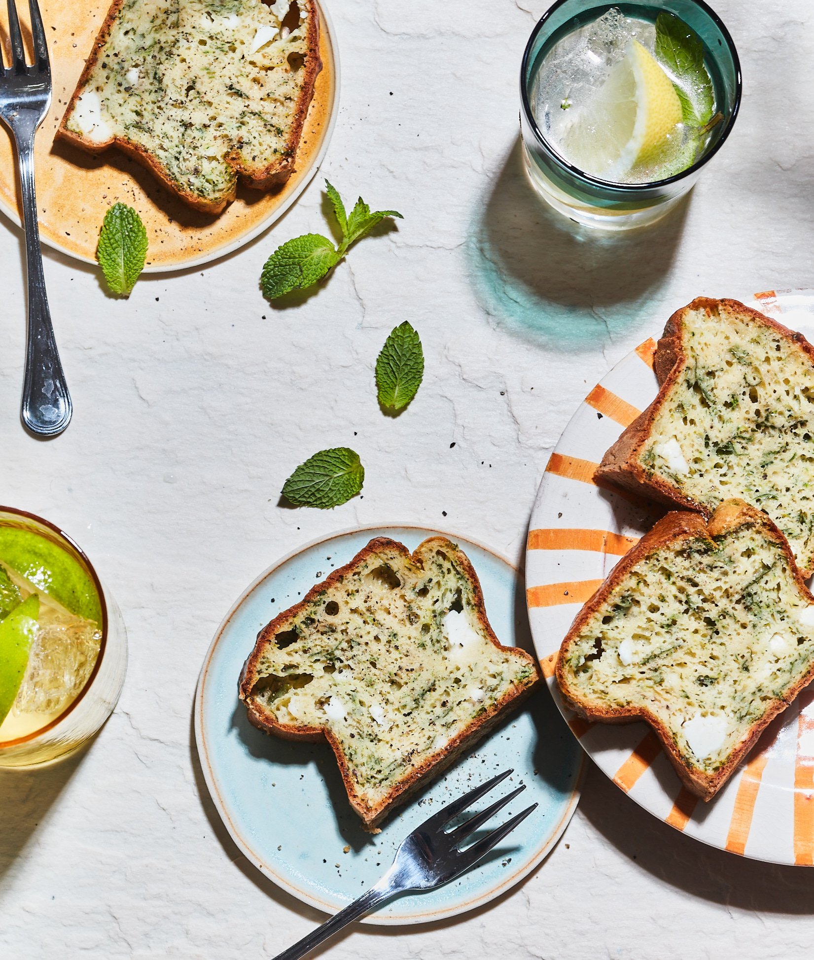 Tranches de pain à l'ail, herbes et fromage sur des assiettes, accompagnées de verres d'eau citronnée à la menthe et un citron.