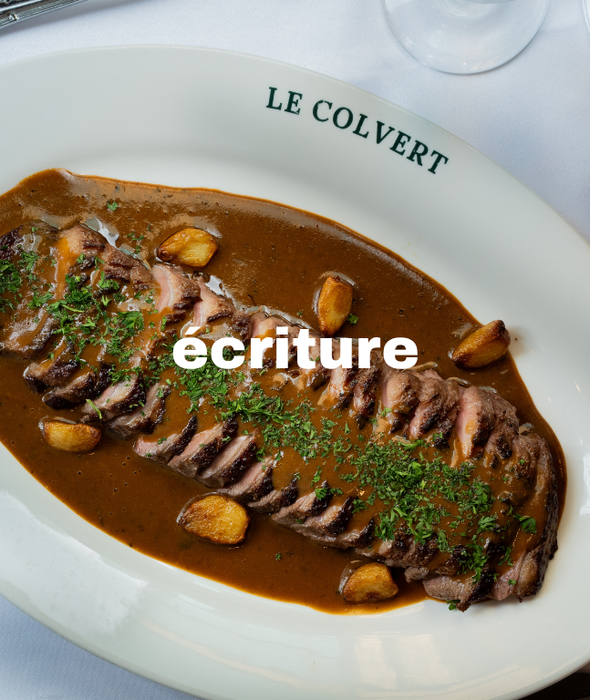Plat de viande en sauce avec des gousses d'ail, servi dans une assiette blanche portant l'inscription 'Le Colvert'.