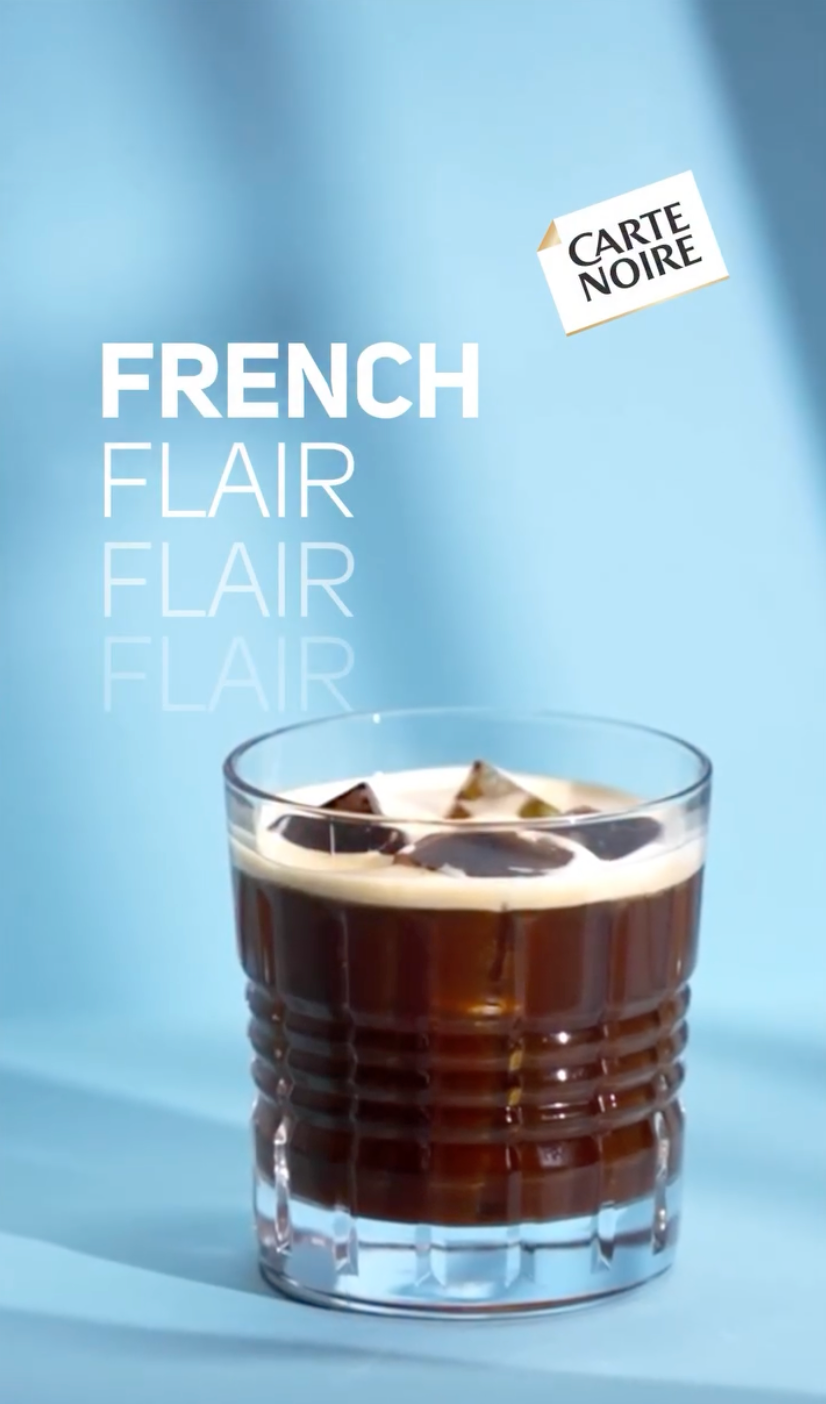 Un verre de cocktail au café crème avec des glaçons, sur un fond bleu avec le texte 'French Flair' répété plusieurs fois et un sticker 'Carte Noire'.