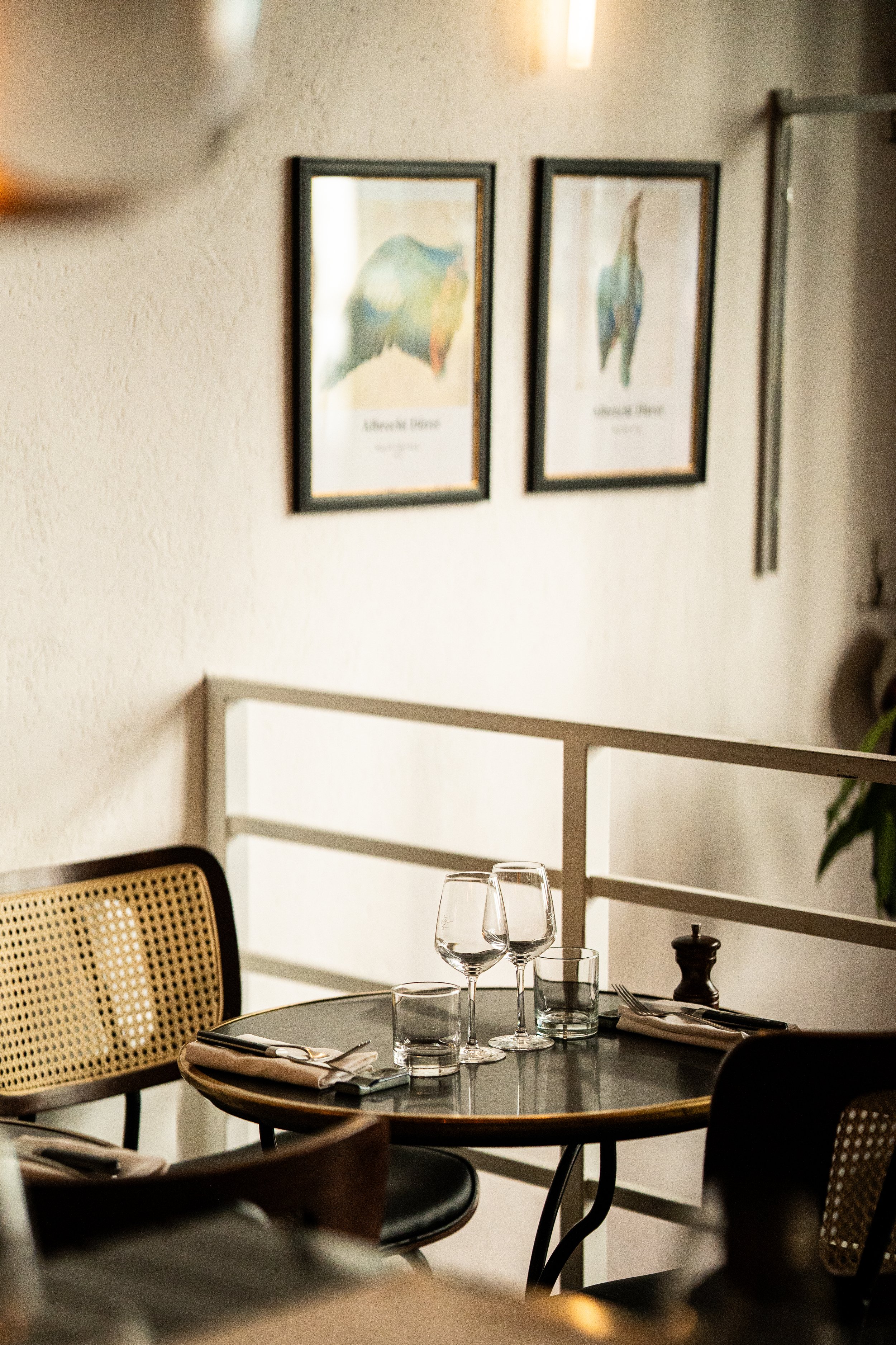 Table à manger avec assiettes, fourchettes, couteaux, verres et gobelets en cristal, dans un restaurant élégant, décor avec deux tableaux d'oiseaux sur le mur