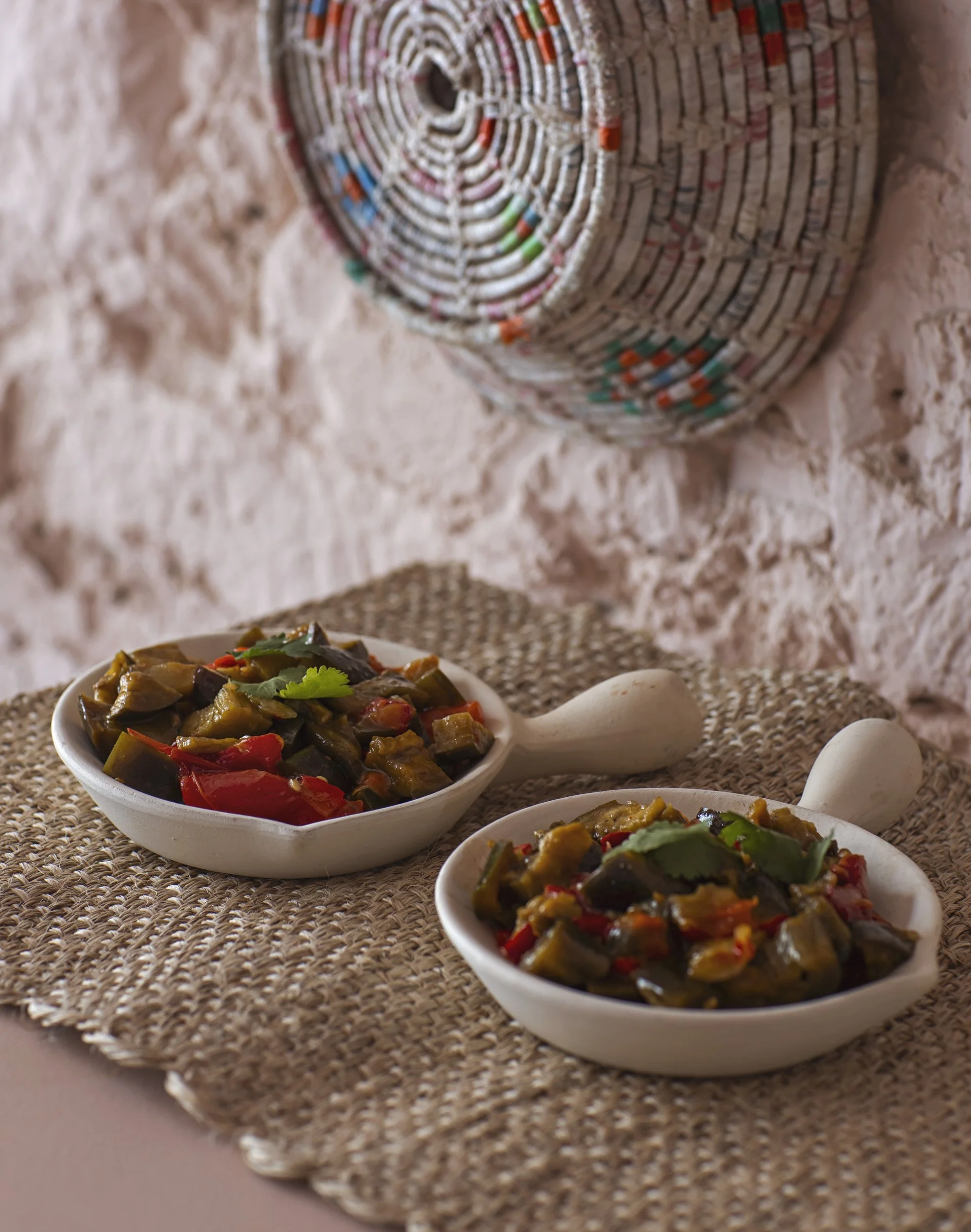 Assiette de légumes mijotés avec grains dans un bol blanc, deux œufs crus à côté, sur un tapis en rotin, avec un rouleau de papier toilette en arrière-plan.