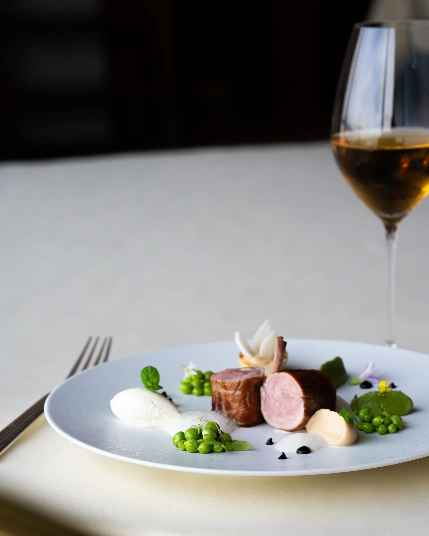 Assiette gastronomique avec viande, légumes verts, purée, assaisonnements et décoration florale, accompagnée d'un verre de vin blanc.