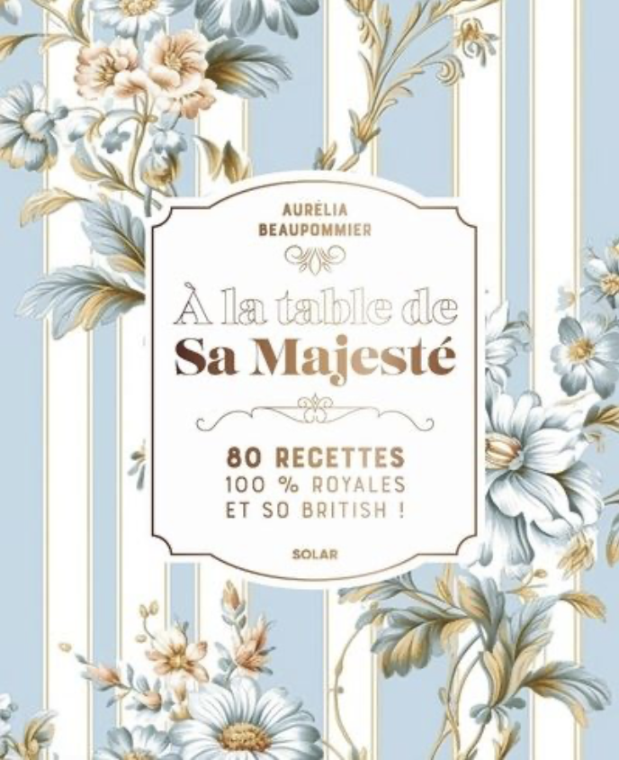 Couverture de livre avec un motif floral bleu et beige, titre 'À la table de Sa Majesté', contenant 80 recettes royales et britanniques, par Aurelia Beaupommier.