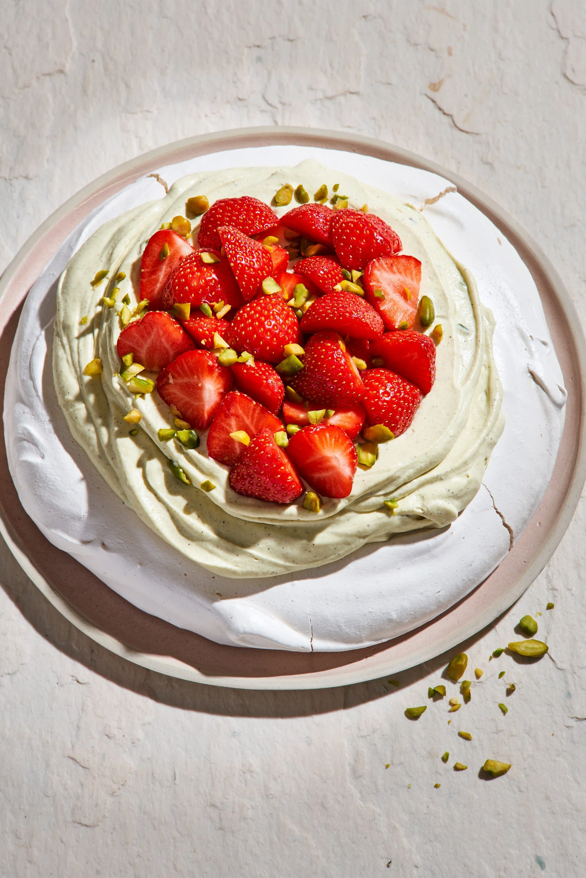 Gâteau avec crème, fraises coupées et pistaches hachées, sur un plateau blanc.