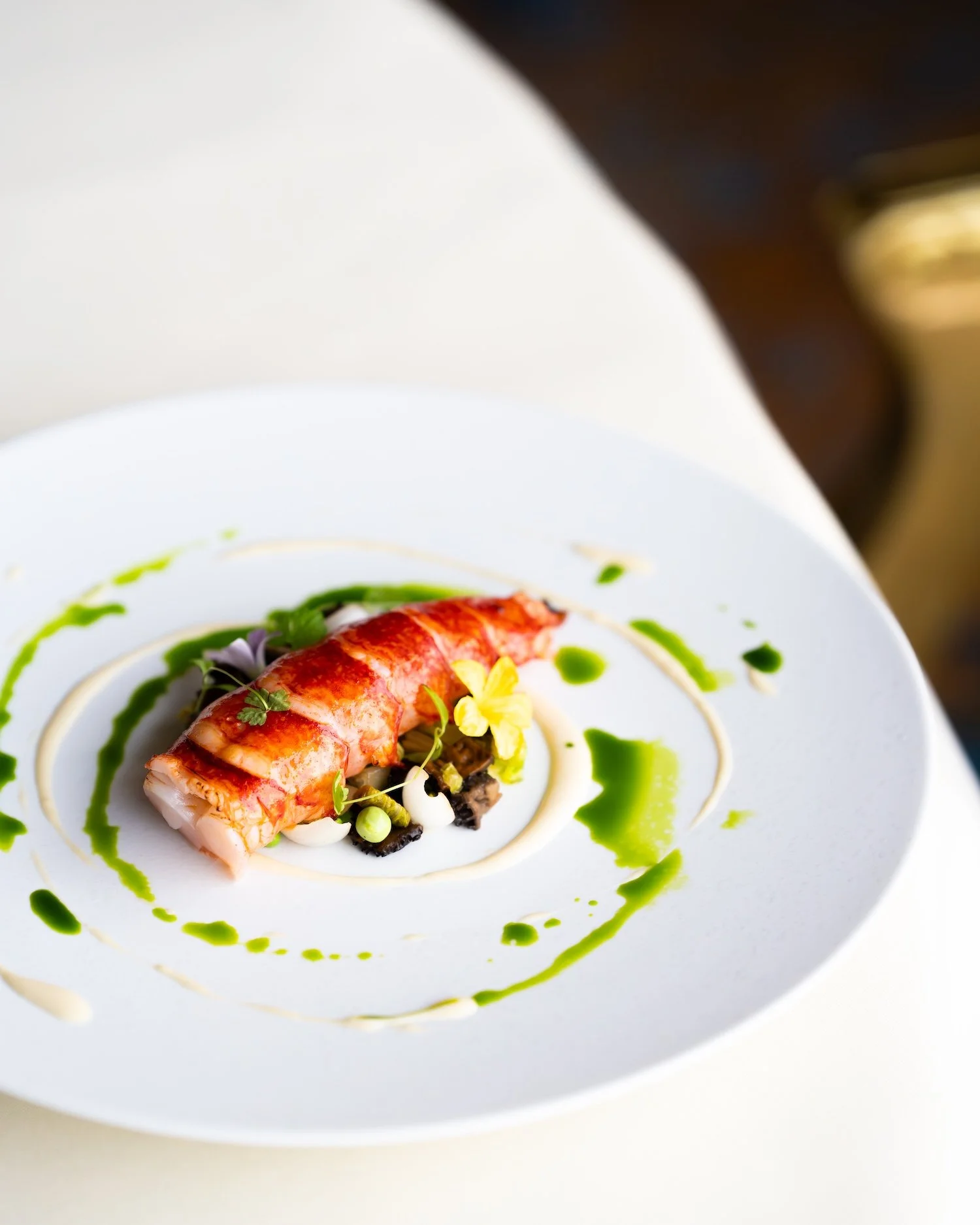 Plat de crevettes avec sauce verte, garnitures et fleurs comestibles, présenté dans une assiette blanche