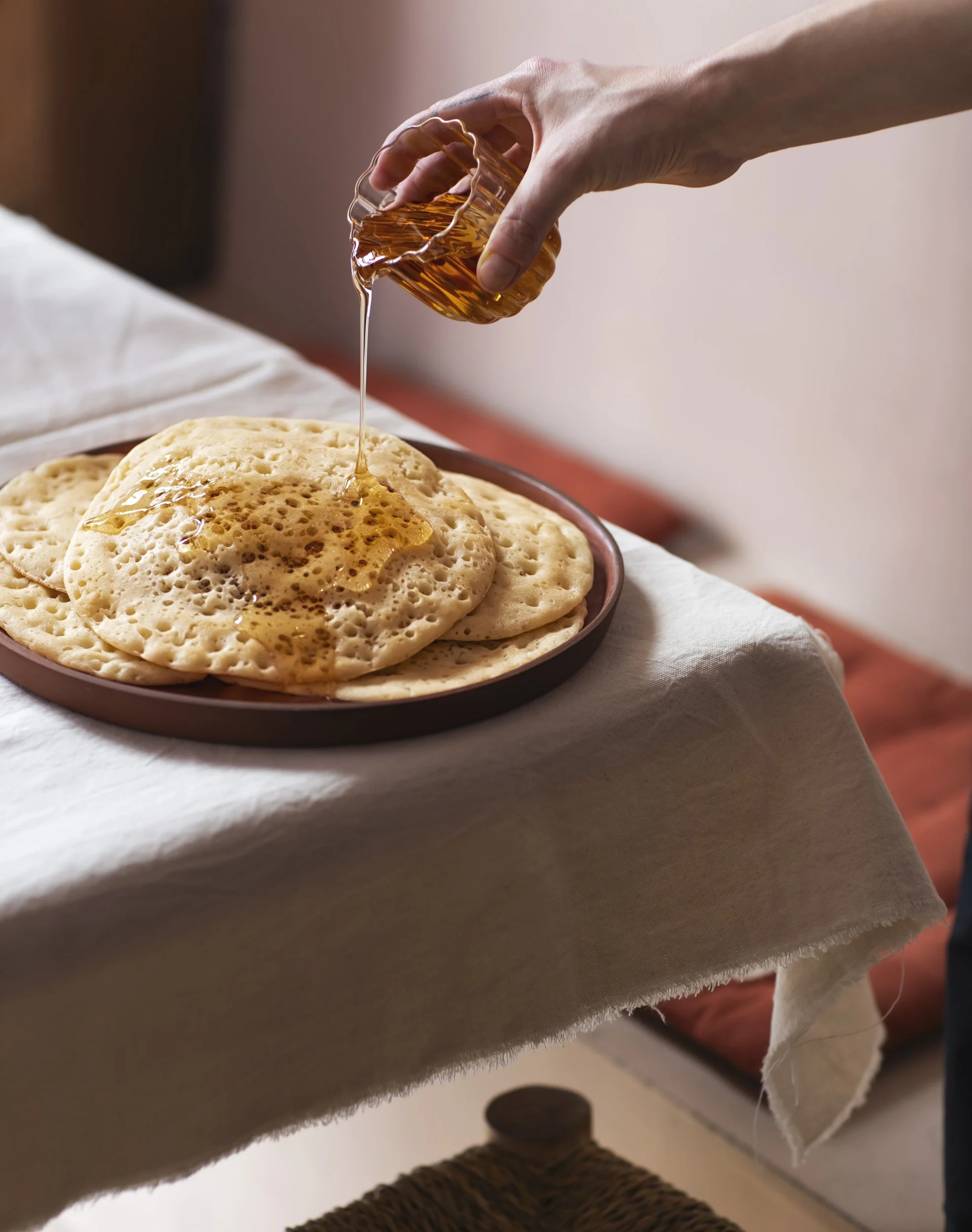 Une main verse du miel sur des crêpes empilées.