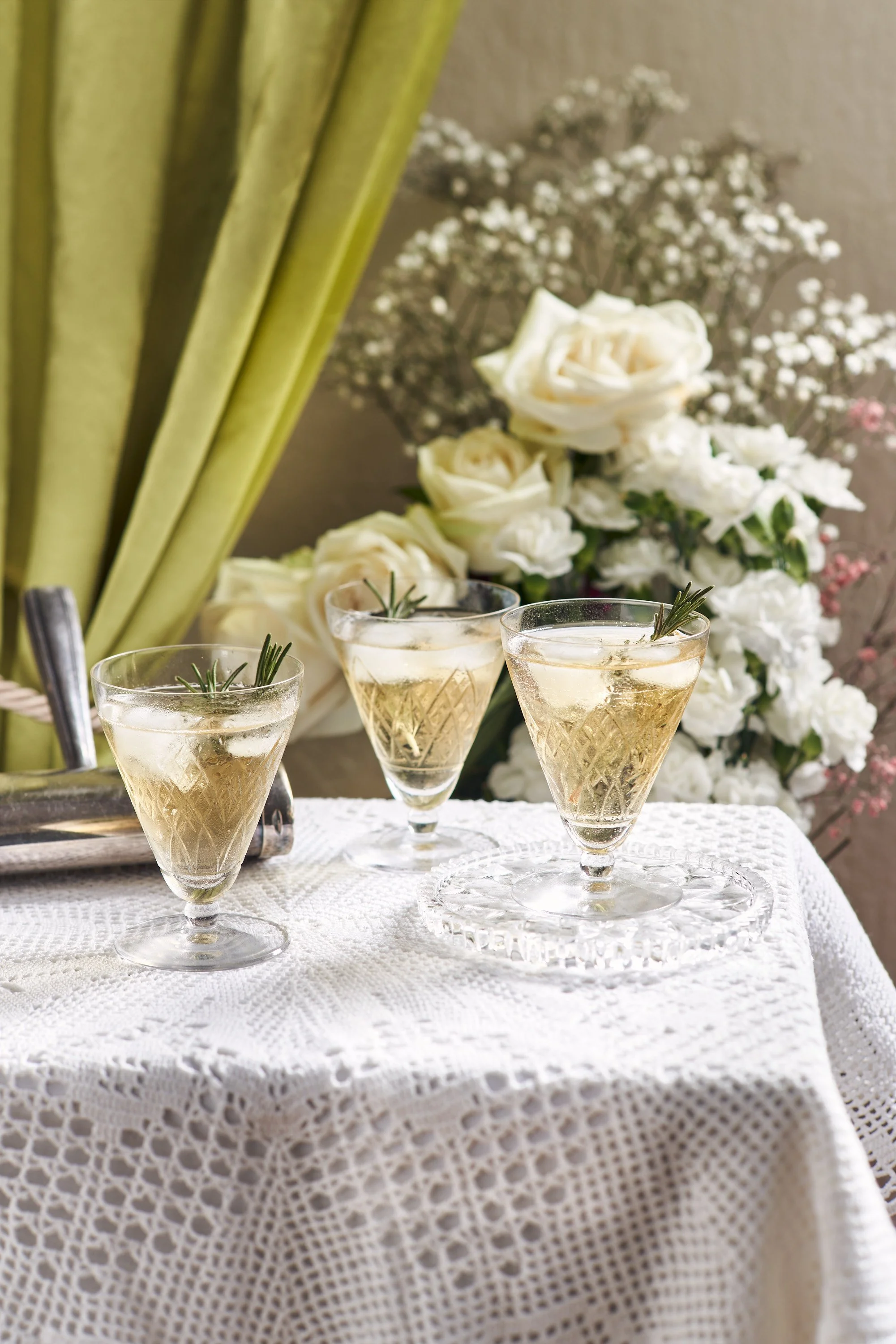 Verres de champagne avec des branches de romarin sur une table en dentelle blanche, décoration florale blanche en arrière-plan.
