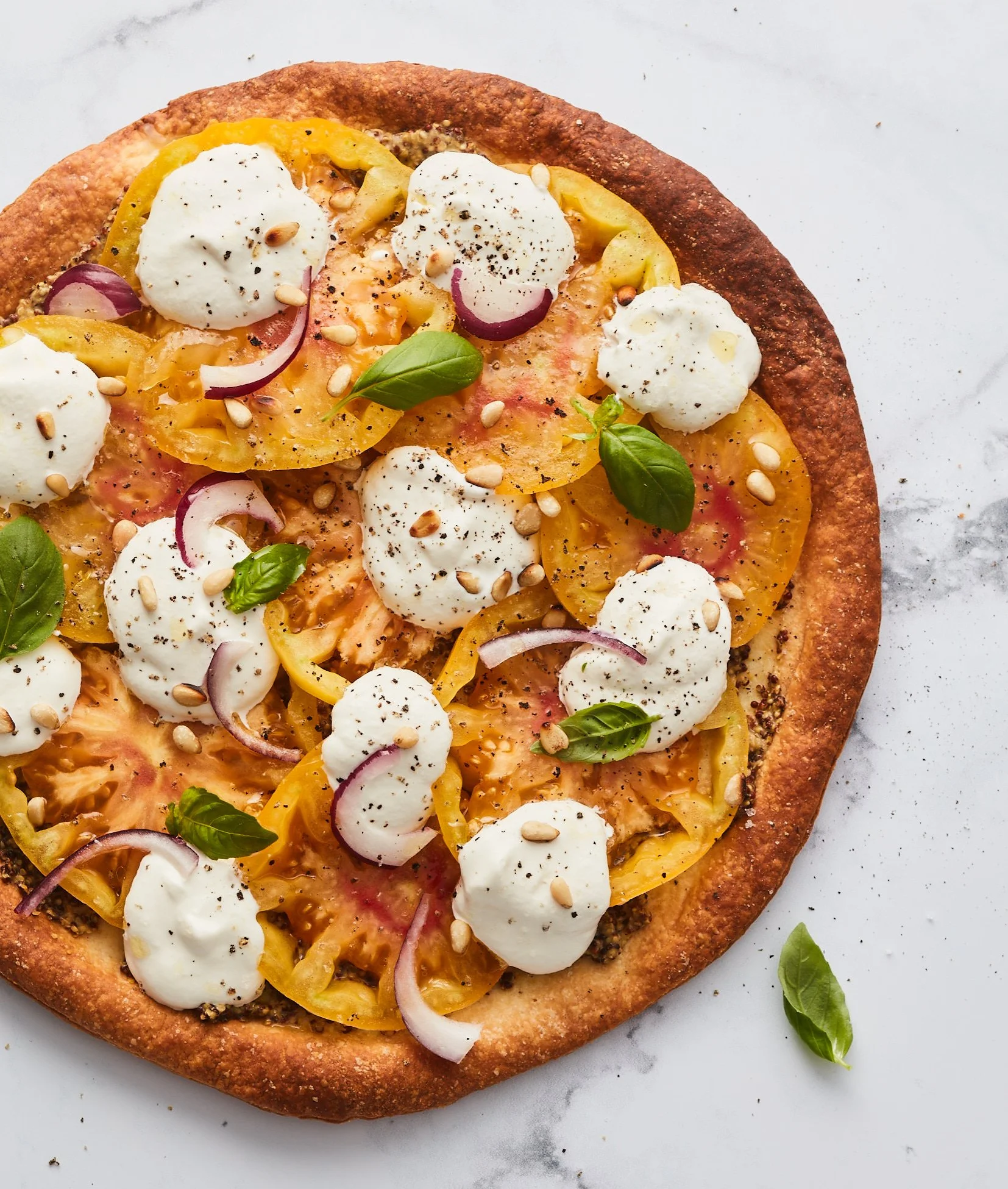 Pizza garnie de mozzarella, tomates jaunes, oignons rouges, basilic, graines de tournesol, poivre noir, et sauce.
